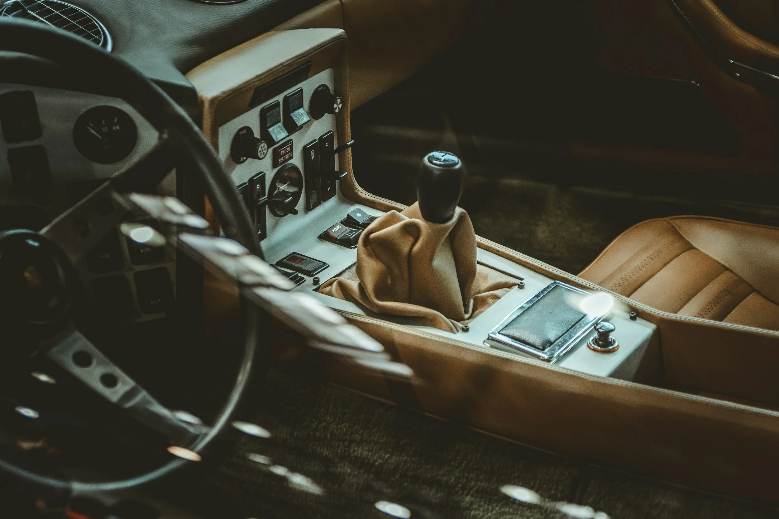 Close-up of vintage car interior showing the gear shift, dashboard with control switches, and leather upholstery in tan and black.