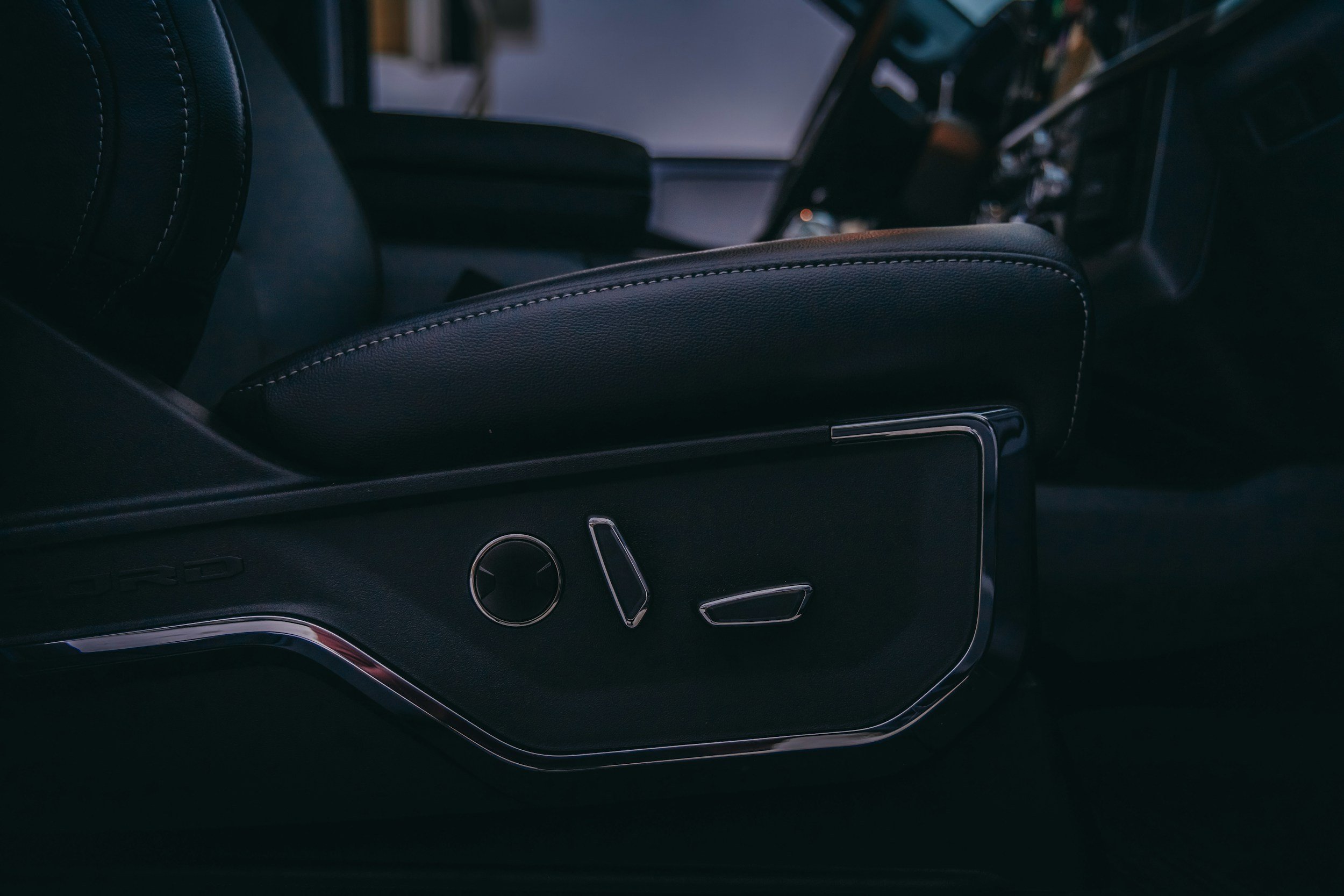 Close-up of a black car's interior showing part of the seat and dashboard with controls.