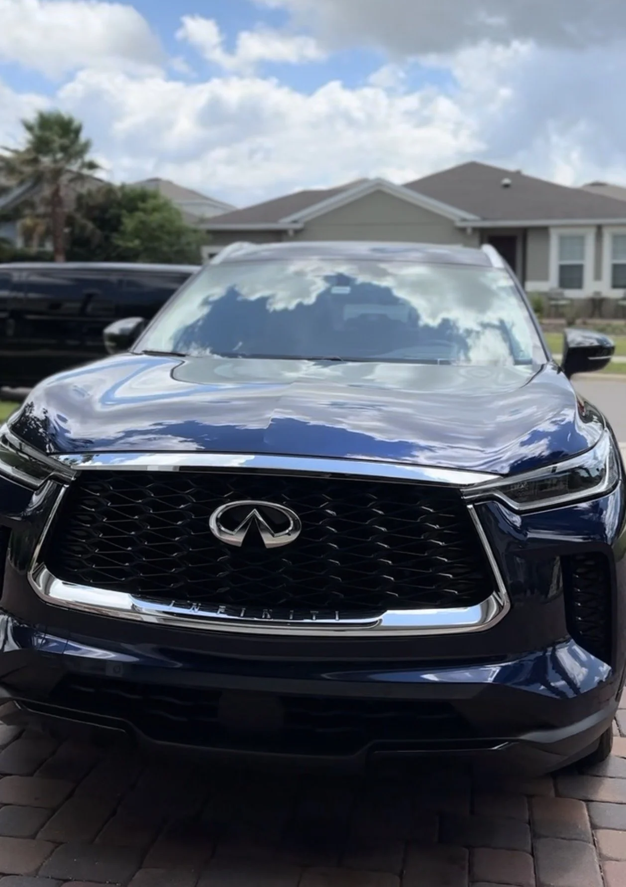 A black Infiniti SUV parked outdoors in front of residential houses under a partly cloudy sky.