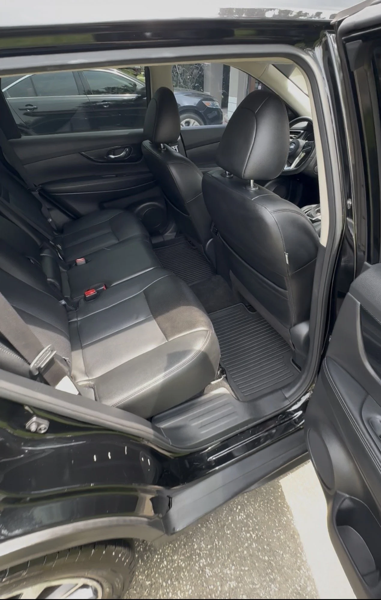 The interior of a black SUV showing the second row seats with black leather upholstery and the front dashboard. The vehicle is parked, and part of a white car is visible through the window.