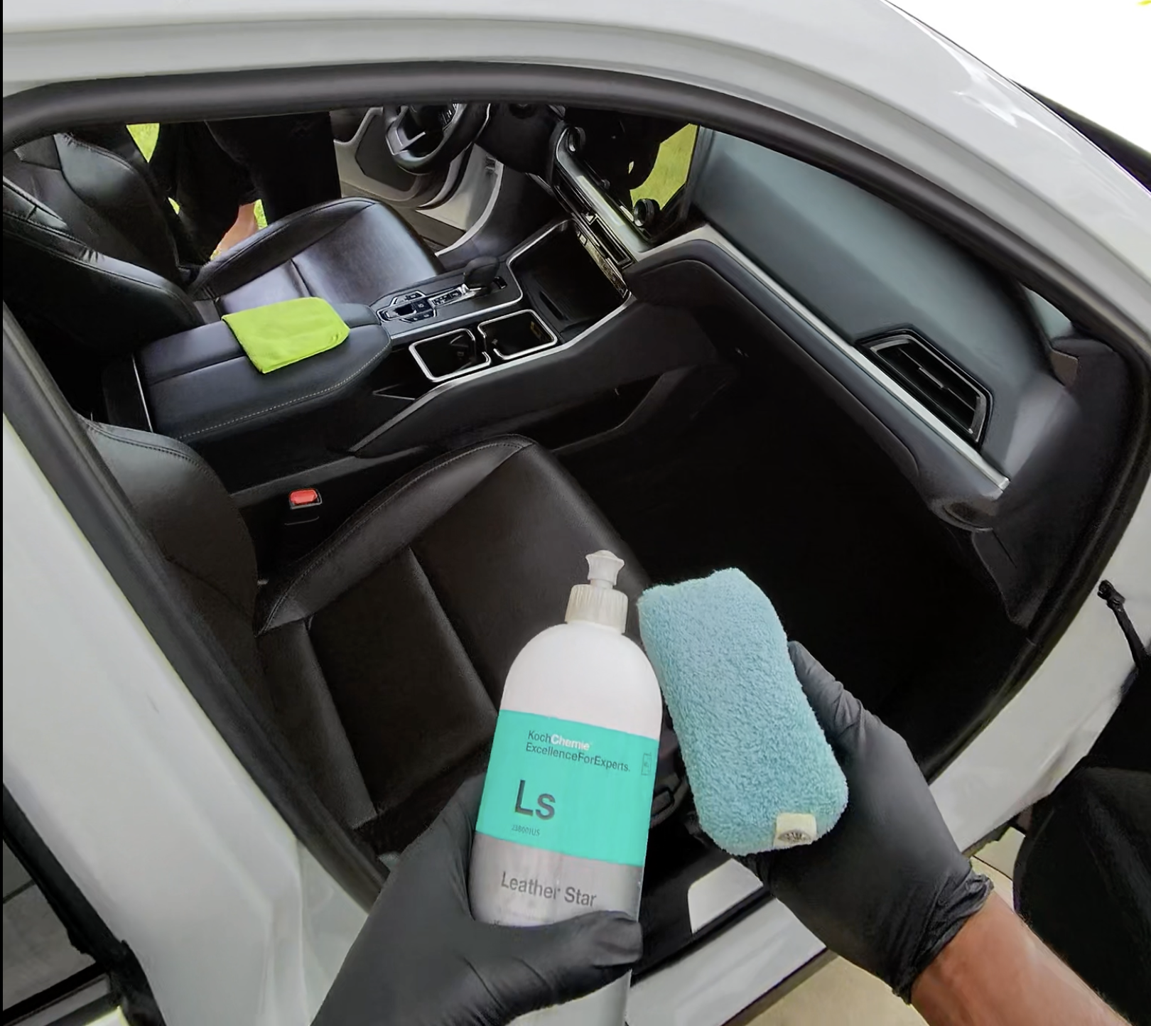 The interior of a car being cleaned, with cleaning supplies and black leather seats visible.