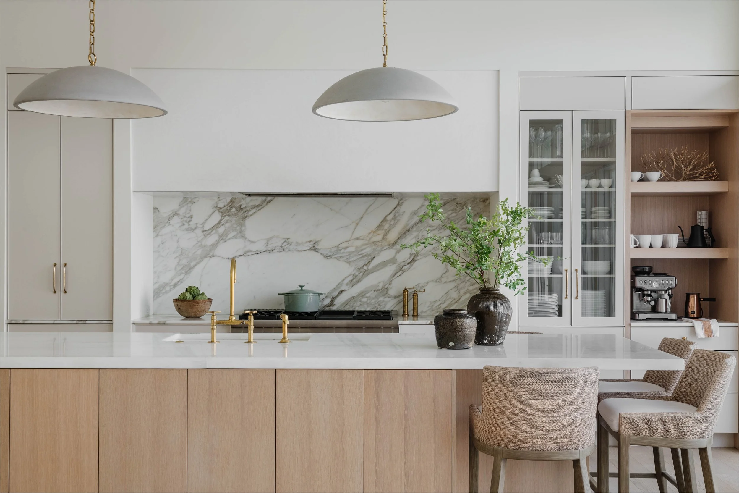 A modern kitchen with bar stools on the side of the kitchen island, wooden cabinets on the island, and white countertops.