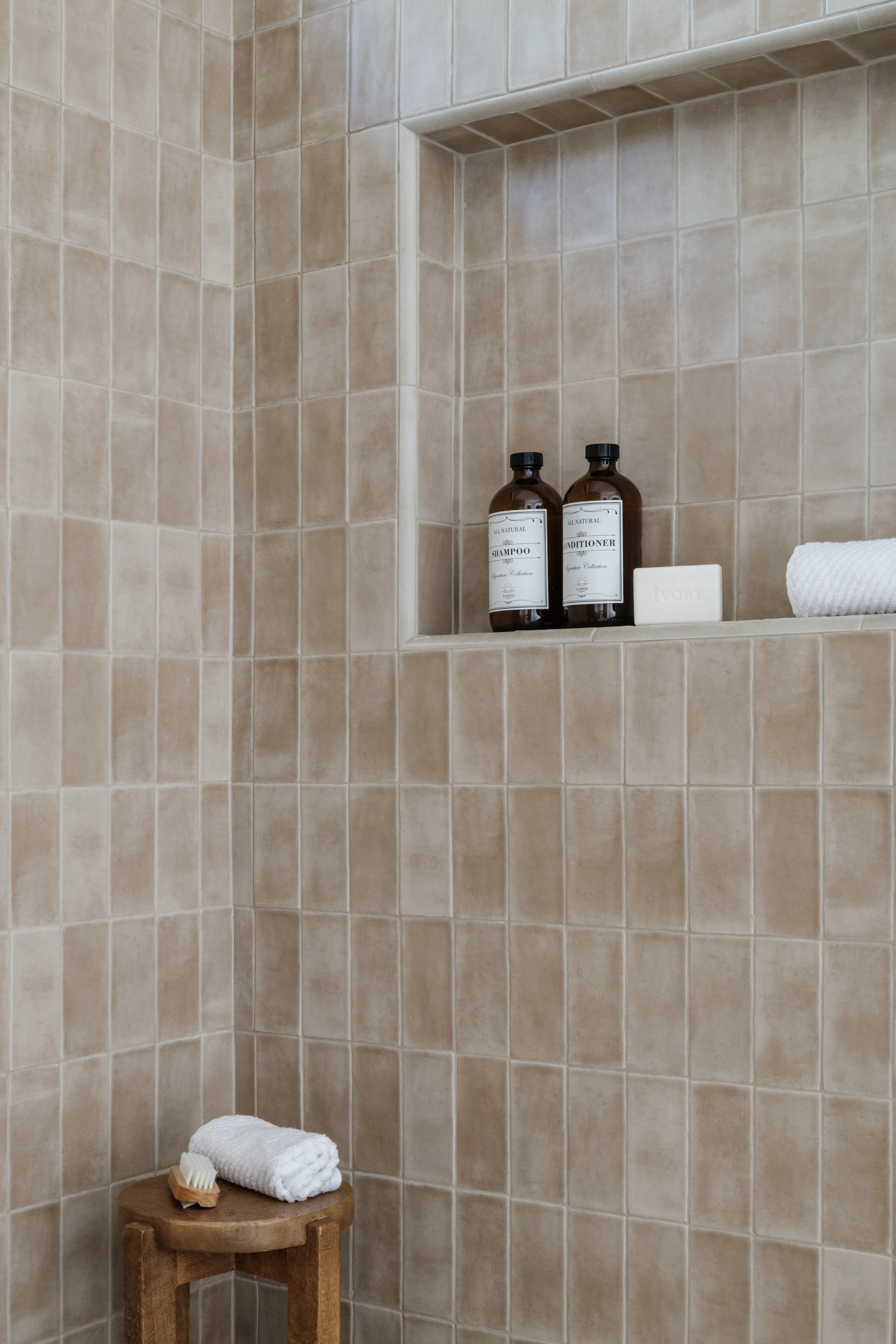 A shower with thin vertical tan tiles