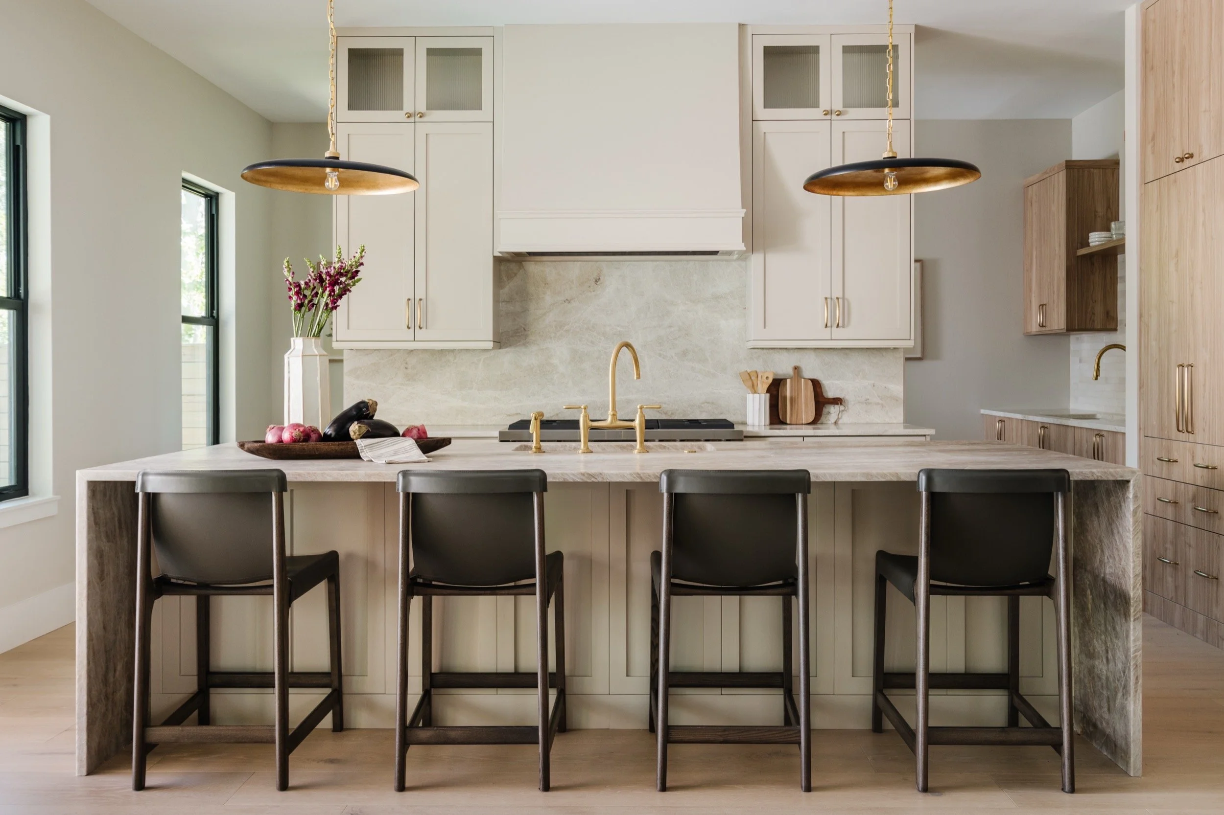 A modern kitchen with ivory cabinetry and a large white kitchen island. Four bar stools. Two gold and black pendant lights.