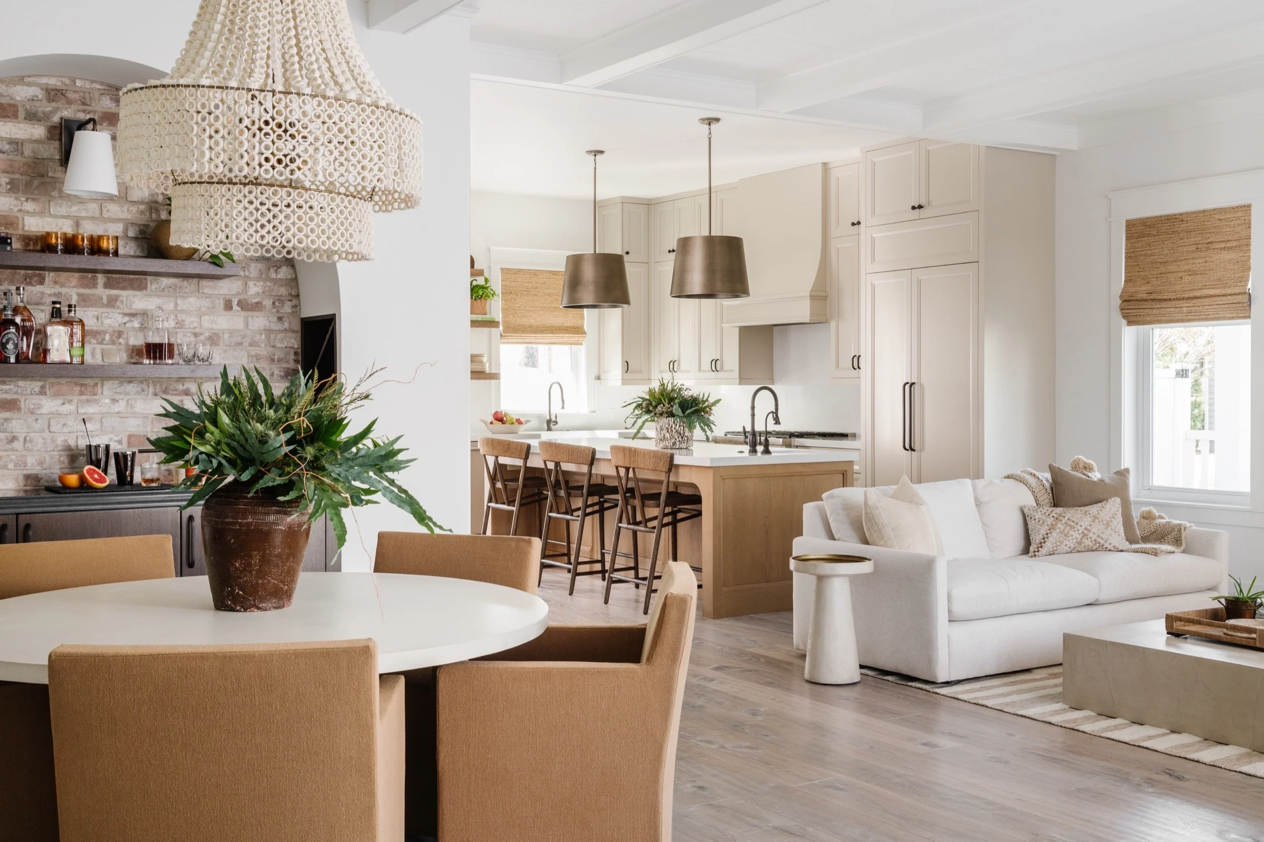 Dining room with white circle table and five tan upholstered dining chairs, a living room with a white cloud couch, and a kicthen with cream cabinets and a large kitchen island.