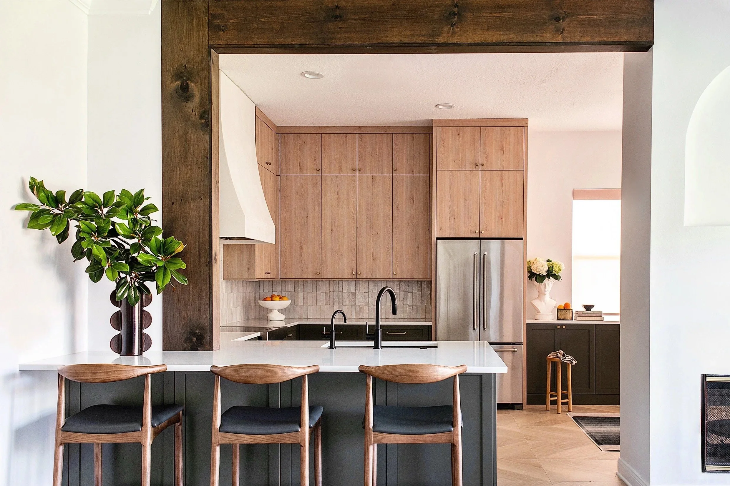 A rustic kitchen with large wooden beams framing the opening. Warm wooden cabinets on the top and darker cabinets on the bottom. 