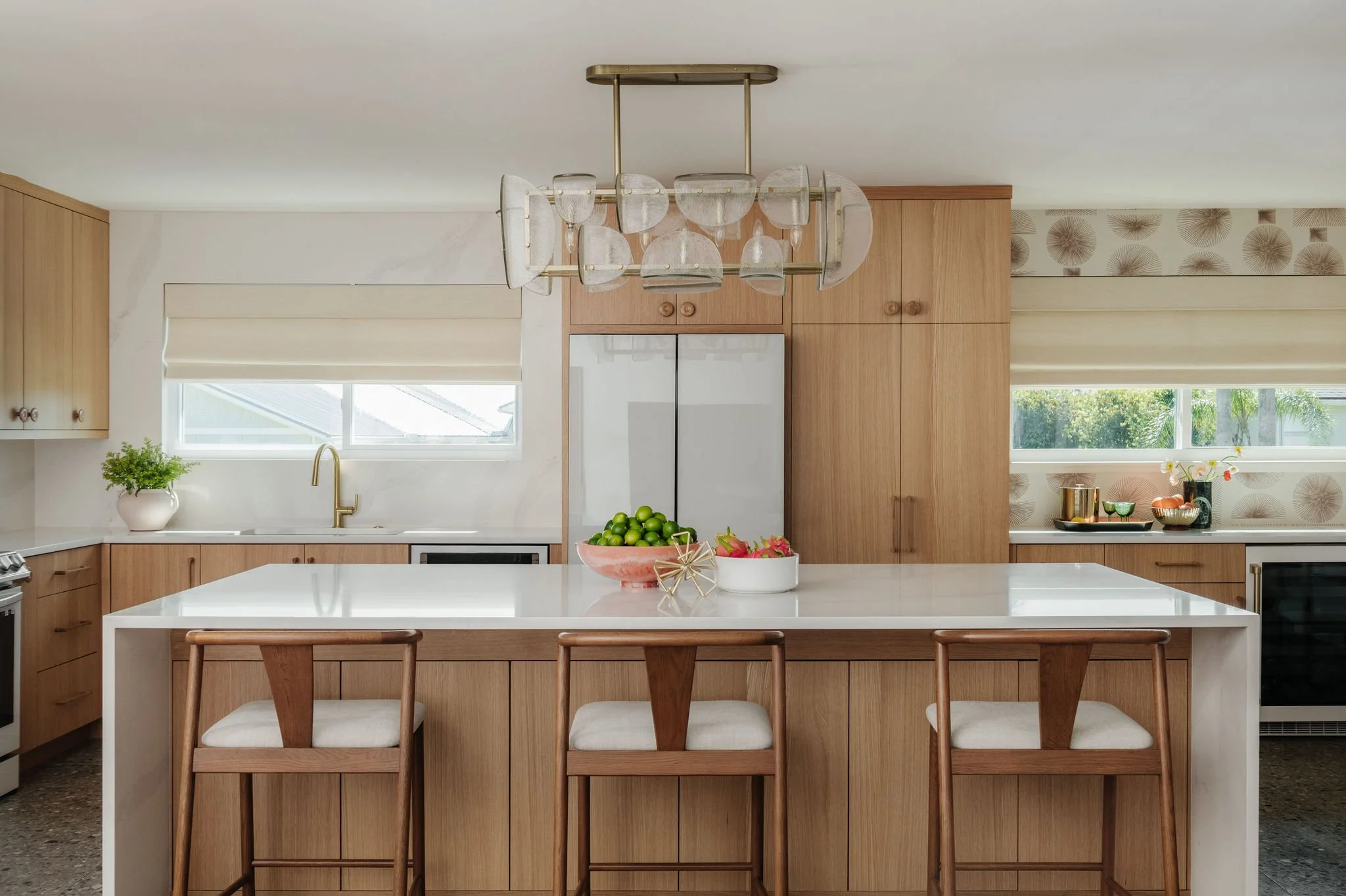 A warm kitchen with light wooden cabinets, white countertops, and a glass pendant light.