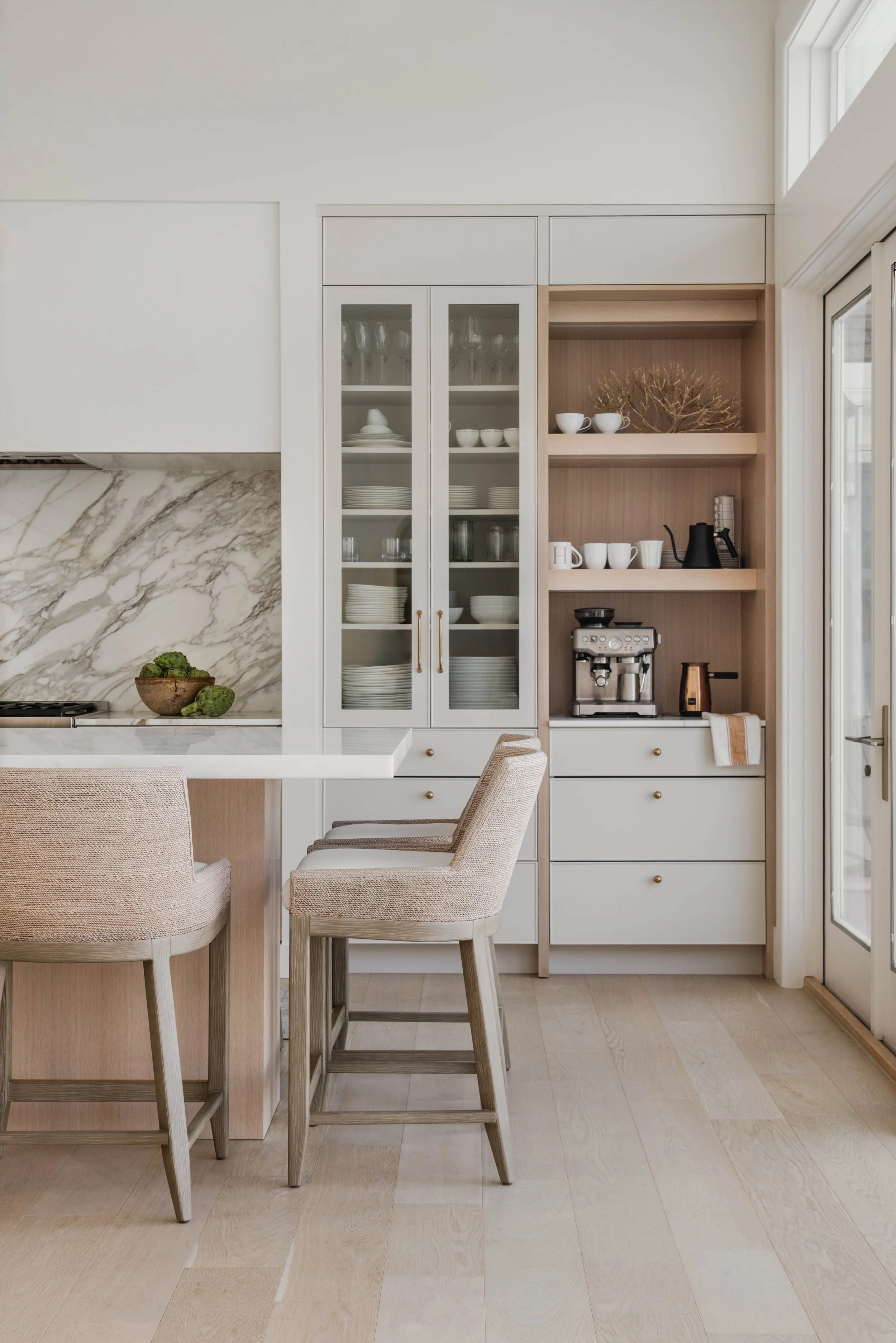 A vingette kitchen photograph with a sliver of the kitchen island peeking in on the left and cabinets behind with glass doors and a coffee bar