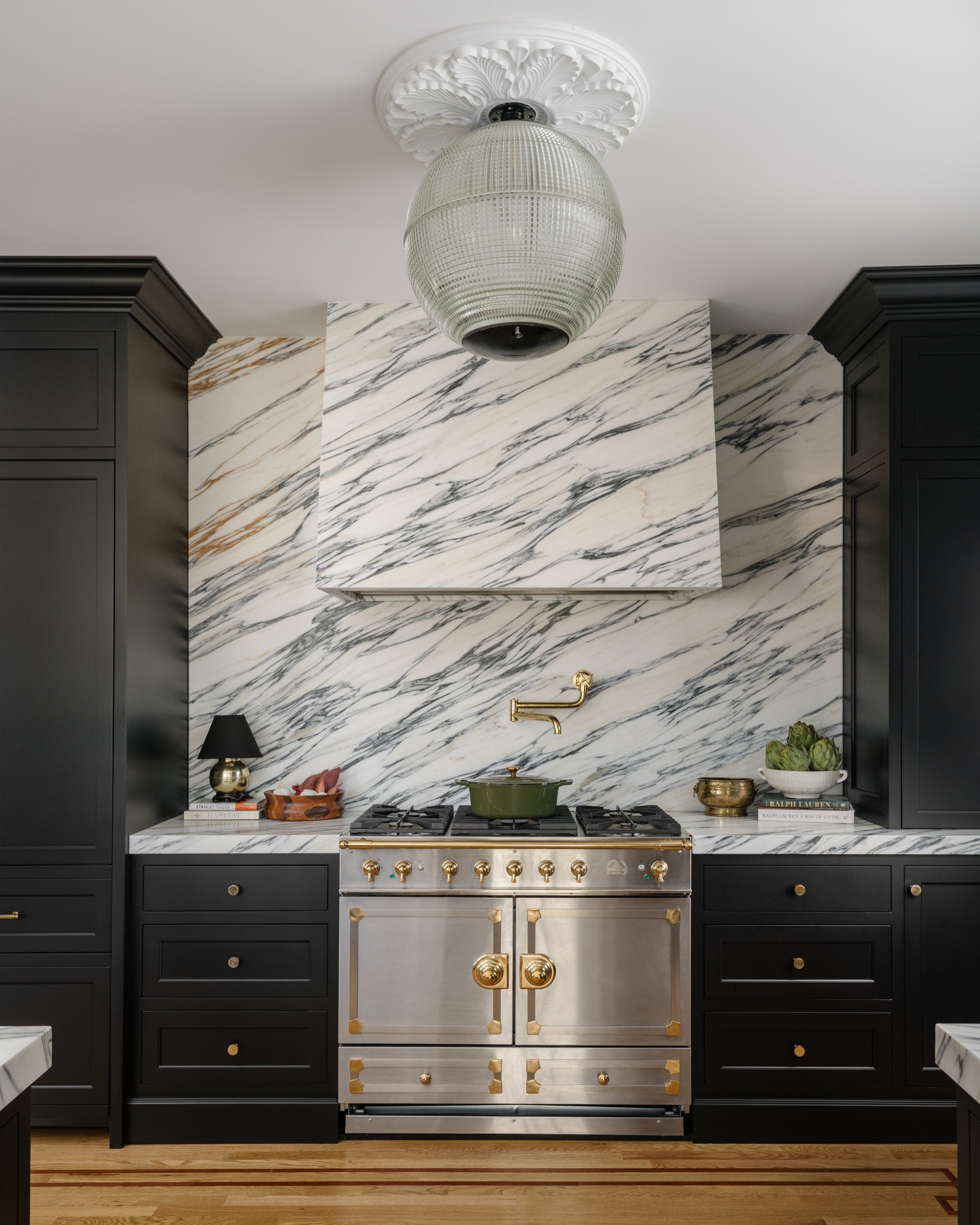 Black kitchen with marble backsplash, and marble range hood.