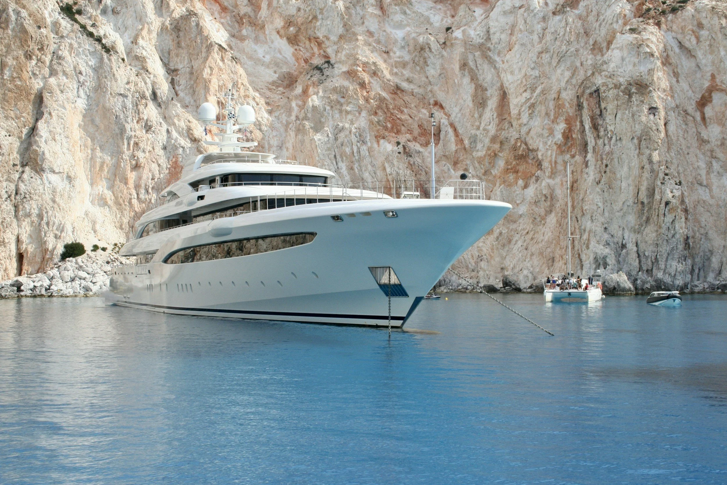 A large white yacht docked in a calm body of water near a rocky cliff.