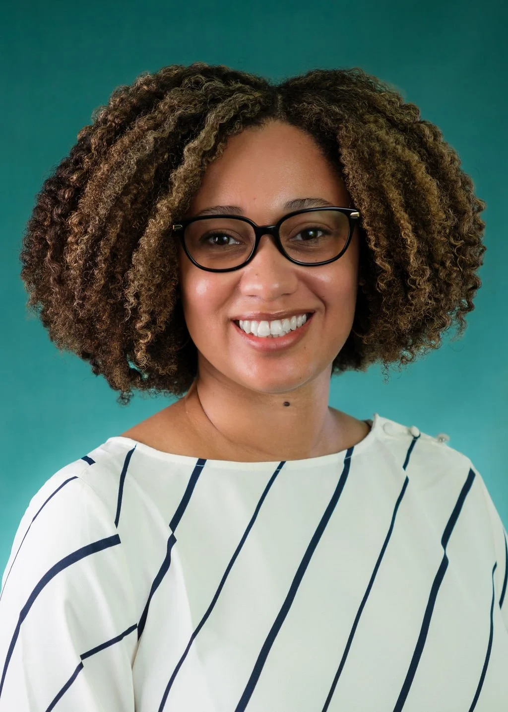 Portrait of a woman with curly hair wearing glasses and a white top with navy stripes, smiling against a teal background.