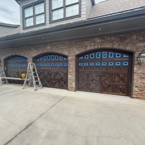 Residential garage doors masked for exterior finish restoration, with ladders in the driveway.