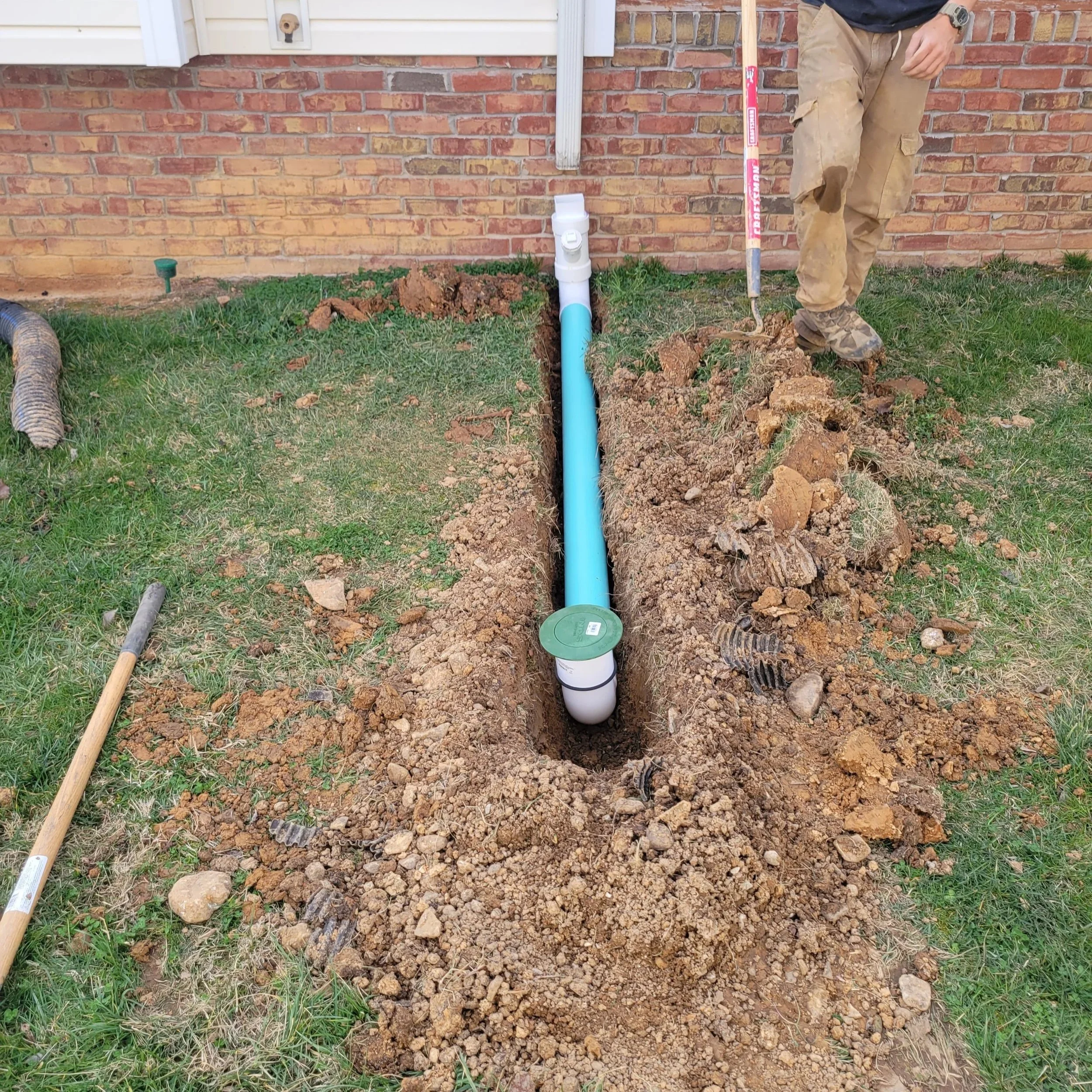 Armor Exteriors technician installing an underground drainage pipe beside a home in Lake Keowee, South Carolina.