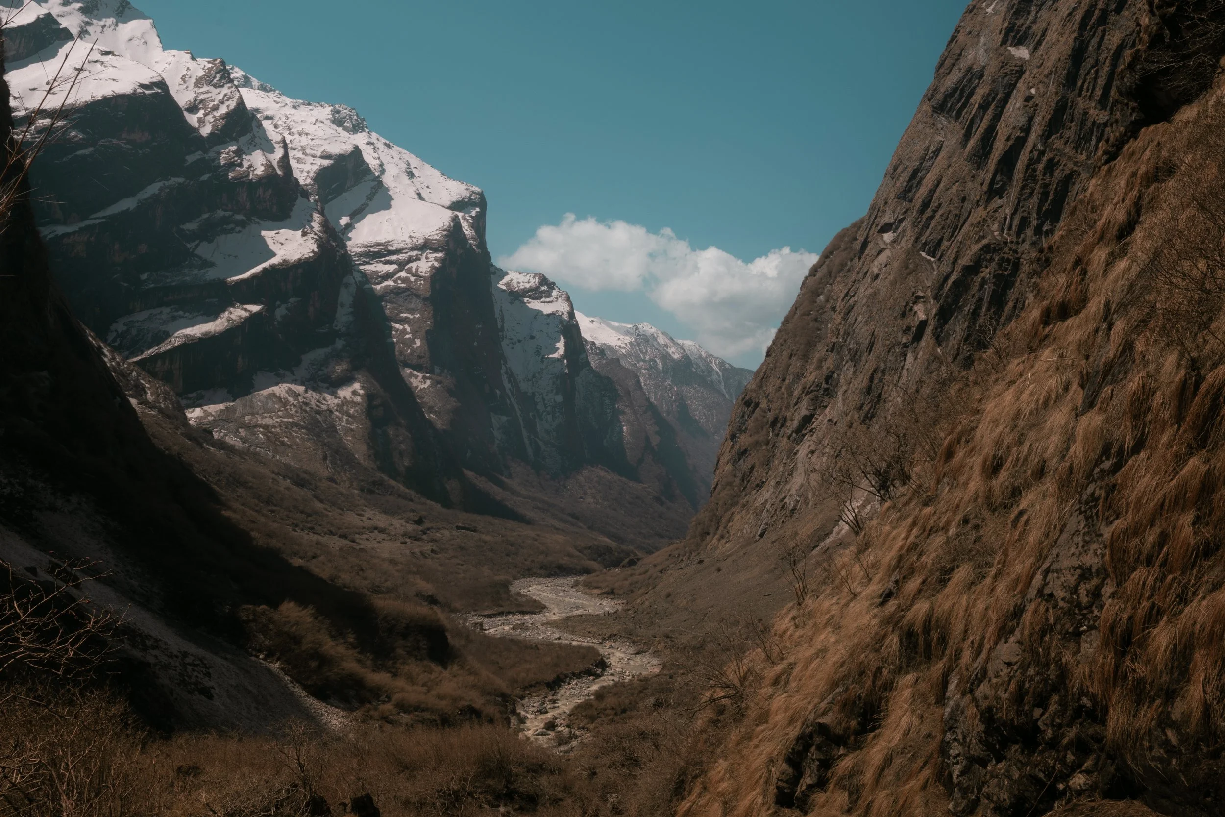 A mountain valley with snow-capped peaks in the background, rugged cliffs on either side, and a small river running through the valley floor.