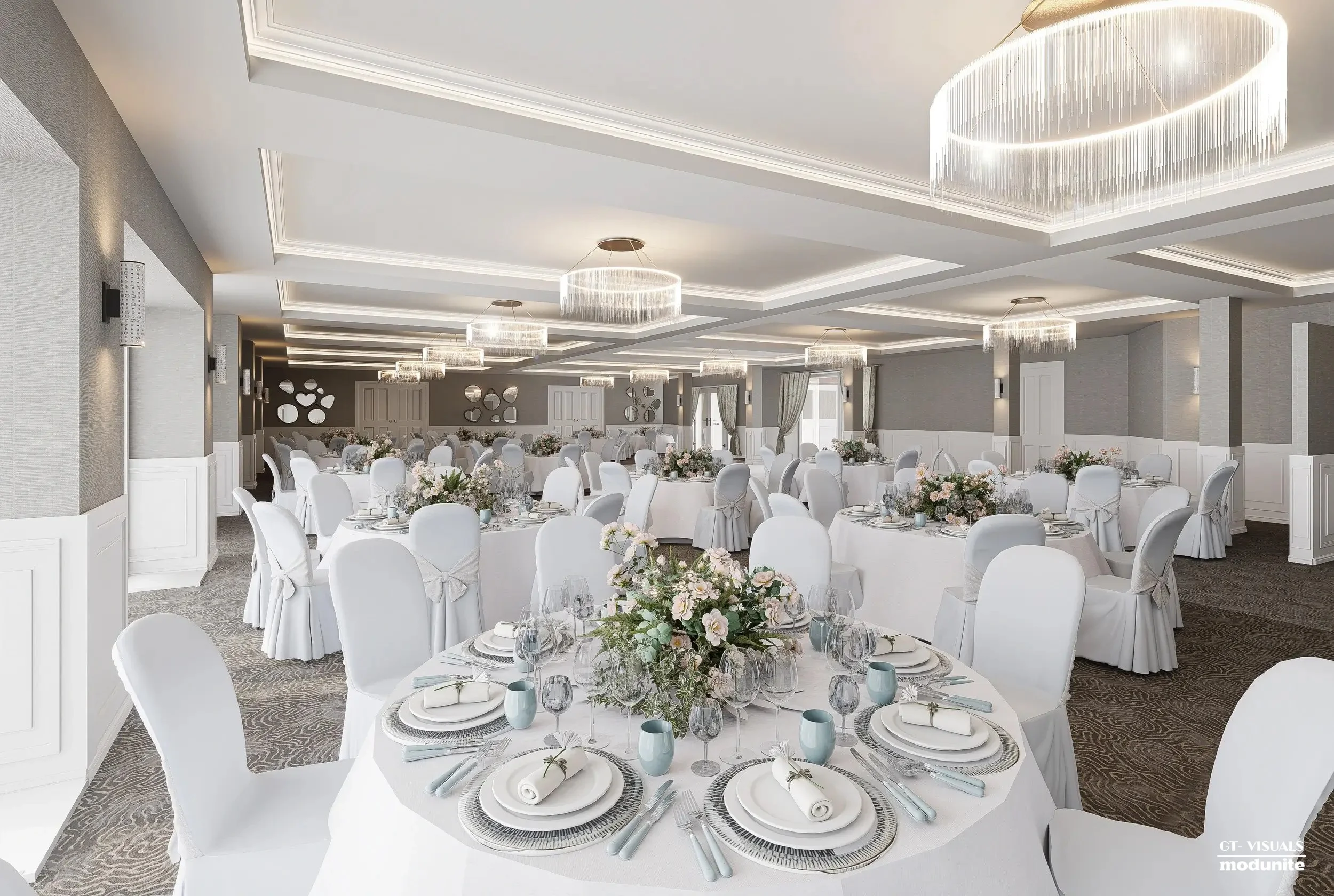 Elegant banquet hall decorated for a wedding reception with round tables covered in white tablecloths, floral centerpieces, and chairs with white covers and bows. The hall features modern chandeliers and gray walls with circular decorative mirrors.