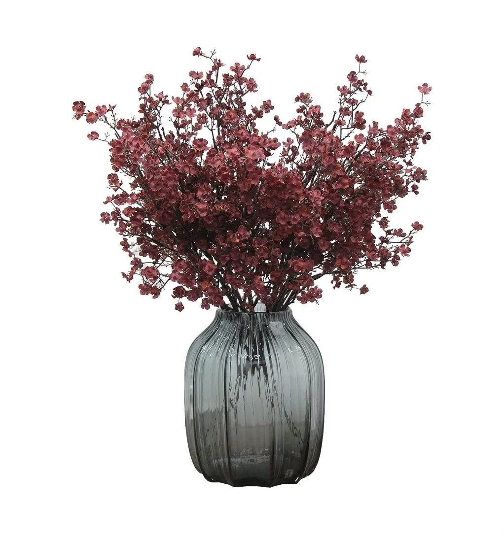 A glass vase with pink flowering branches on a white background.