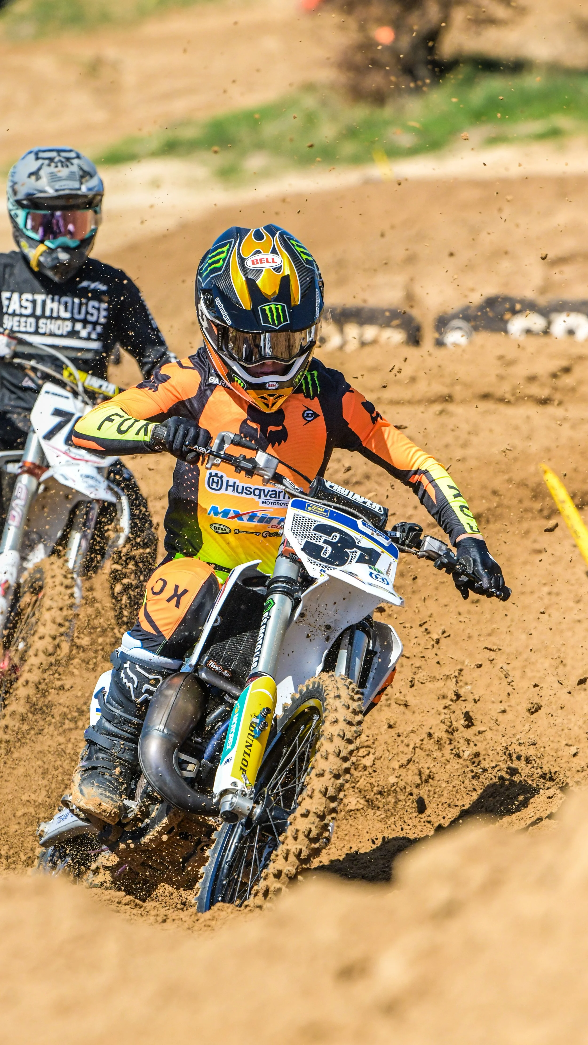 Motocross racers wearing helmets and racing gear navigating a dirt track, kicking up soil.