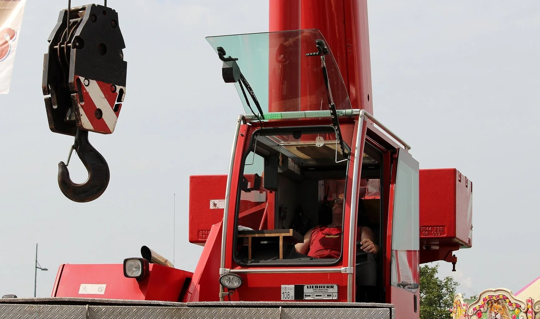 Close-up of a red crane with a hook, operator inside the cabin.