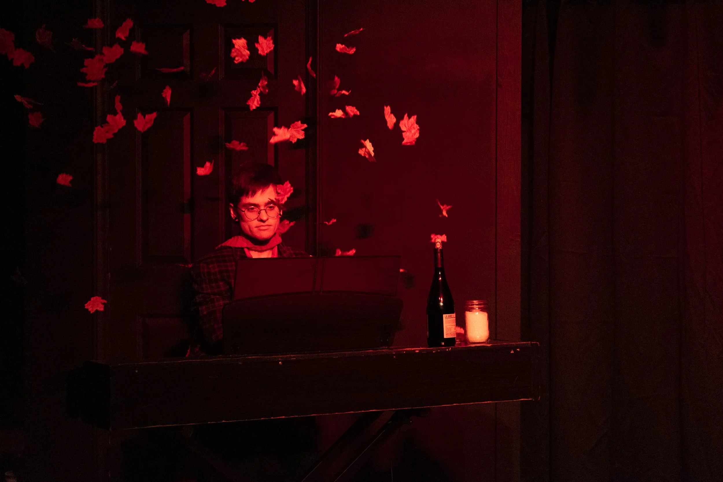 Chris Strauss plays piano at RECITAL. He wears a long red scarf and red leaves fall down overhead.