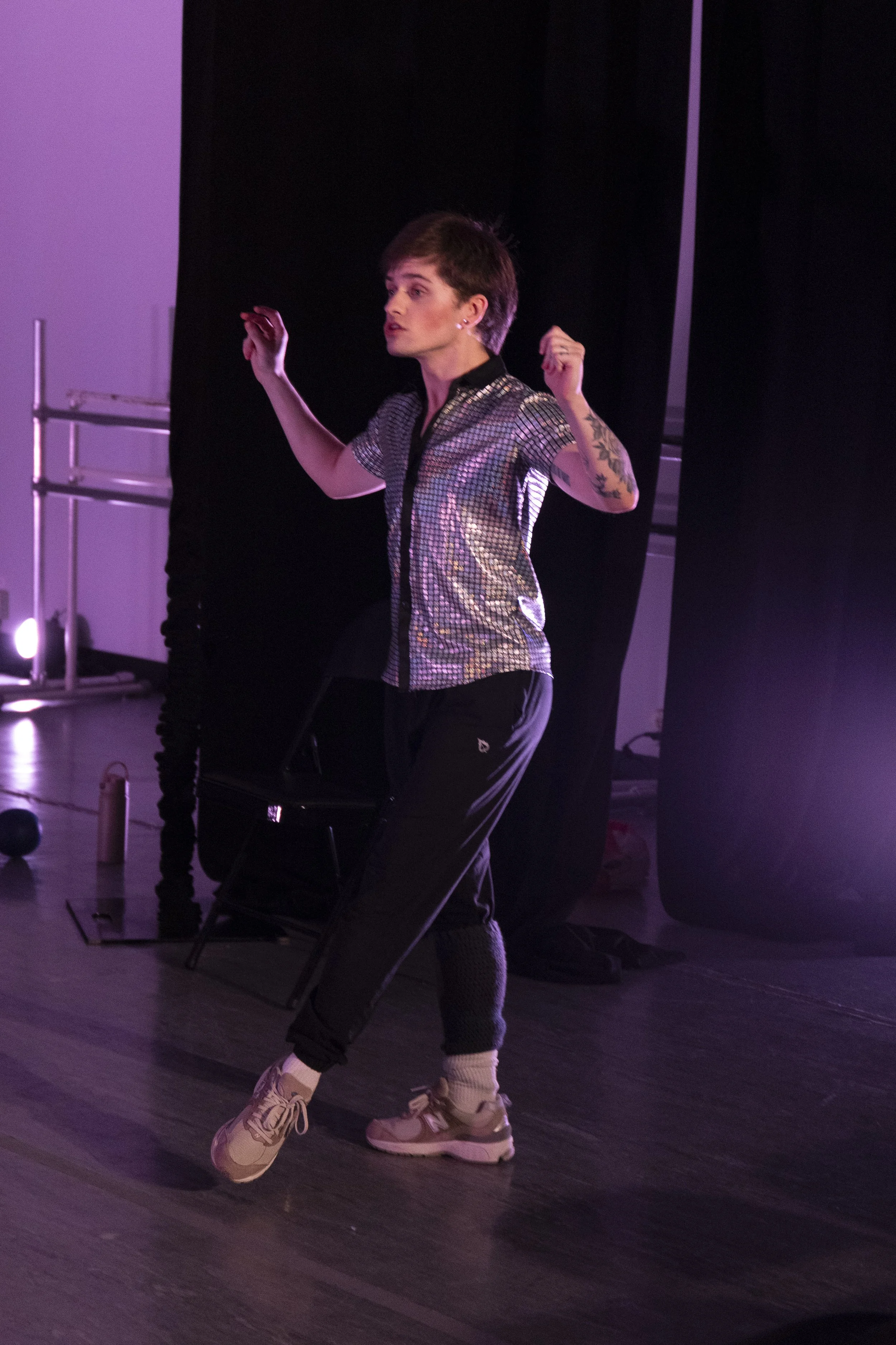 A toxic male dance instructor demonstrates a tendu. His leg is outstretched in front of him on the floor.
