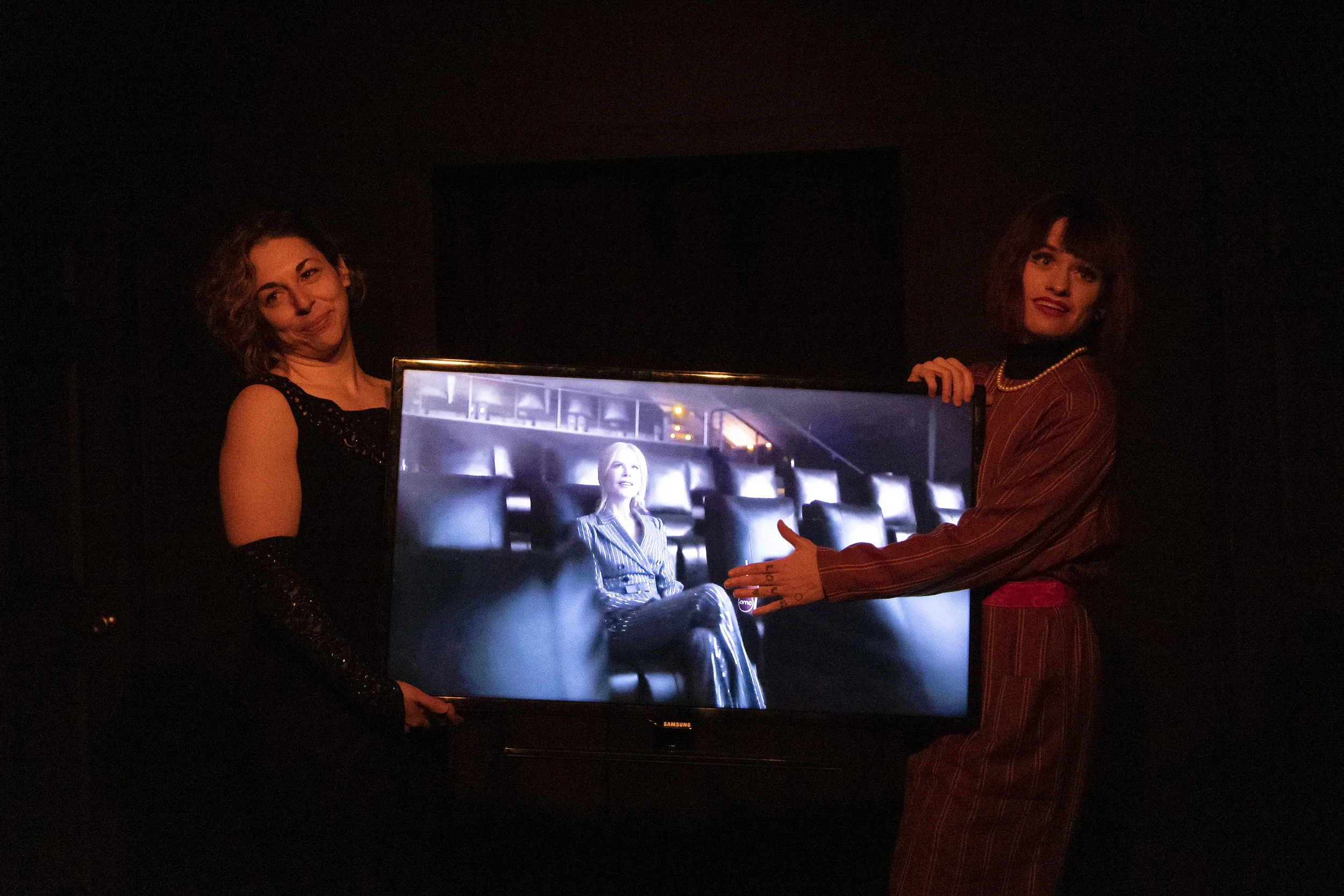 Alyssa Noble and Chriss Strauss hold a TV showing the AMC opening video at RECITAL. 