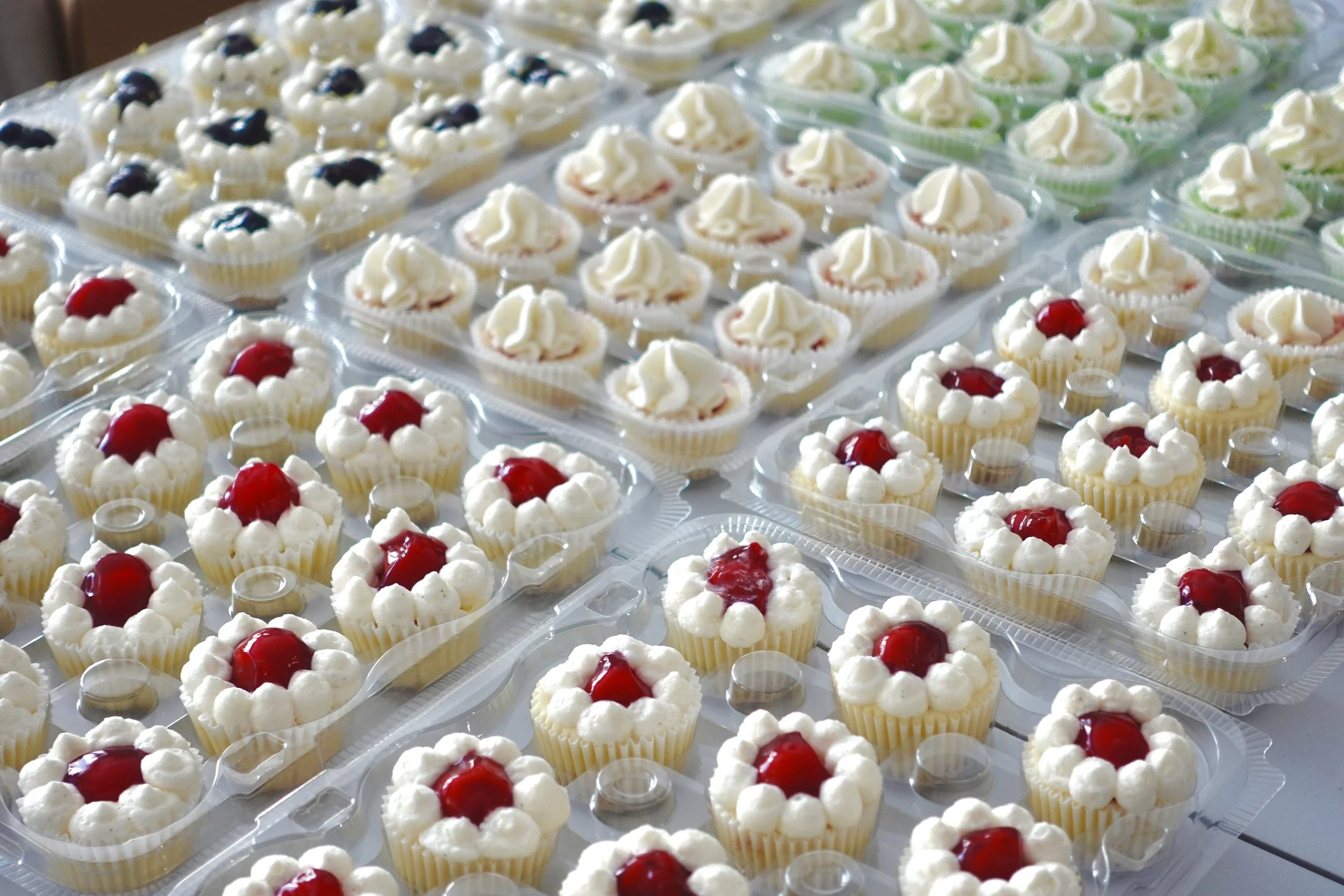 A display of cupcake desserts with white frosting and cherries on top, arranged in clear plastic cups.