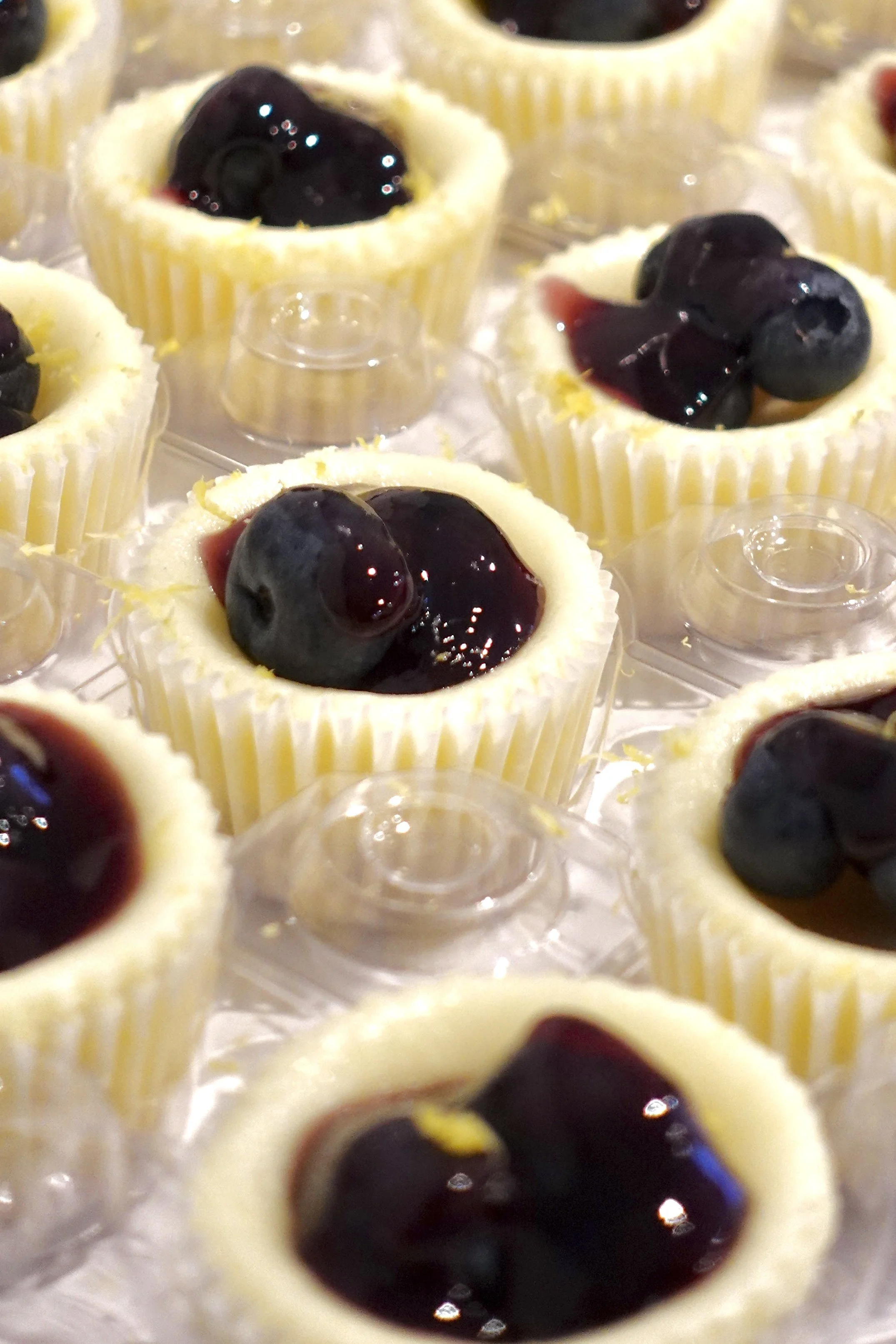 Mini cheesecakes in yellow cupcake liners topped with blueberries and a berry compote.