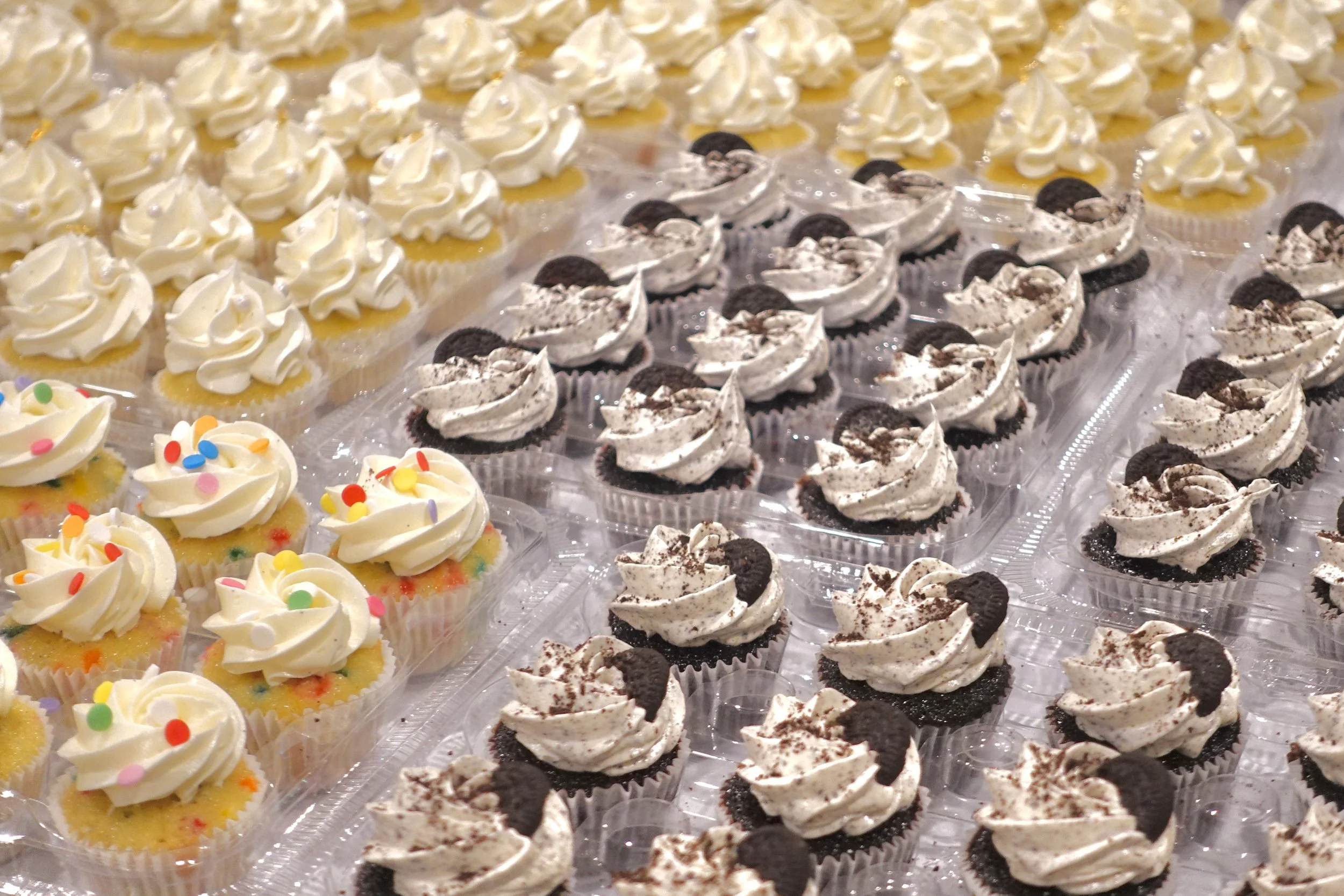 Tray of cupcakes decorated with white frosting, colorful sprinkles, and Oreo cookies.