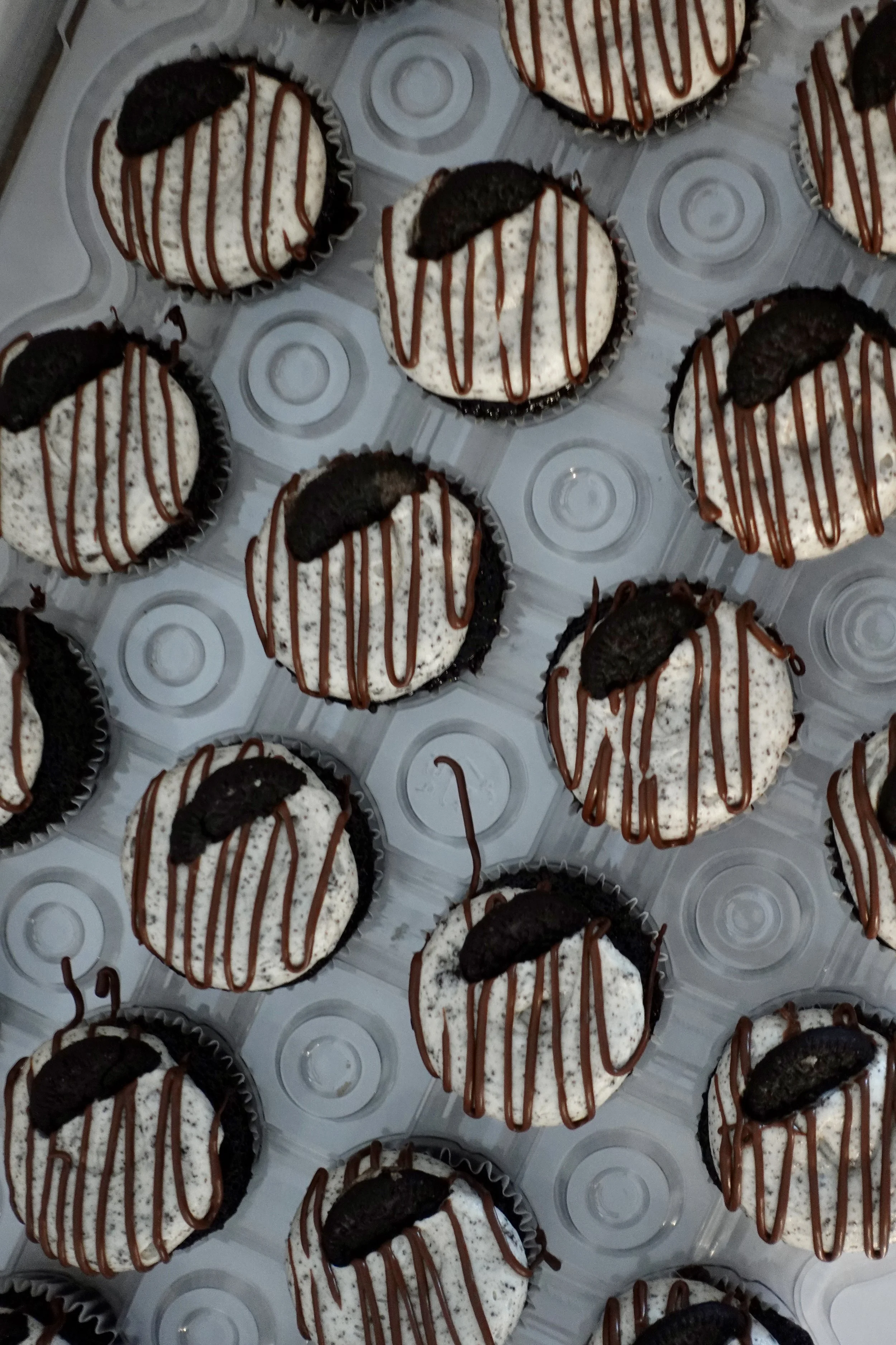 A tray of Oreo cookies topped with Oreo halves, drizzled with chocolate and decorated with white frosting, arranged in individual cups.