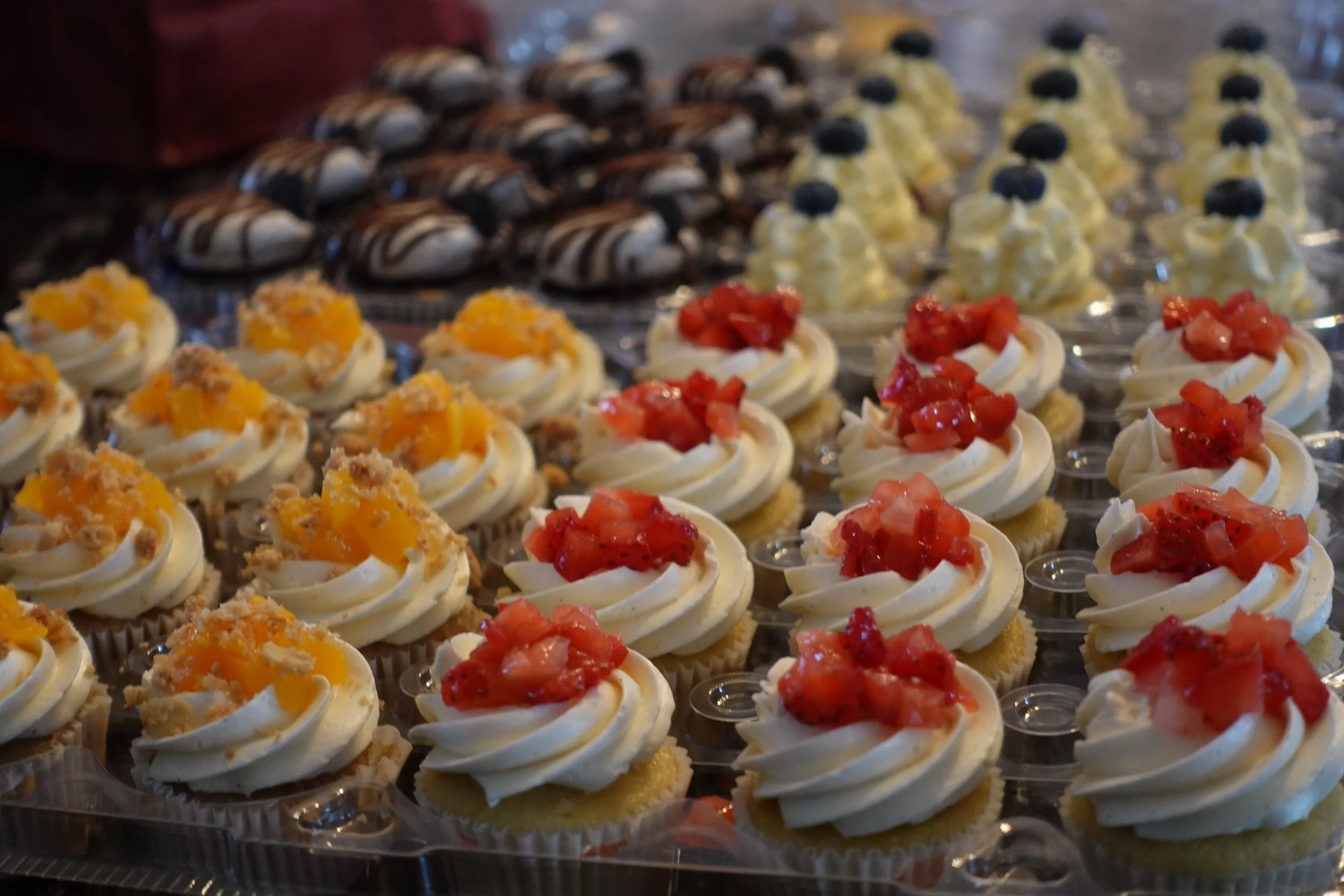 Assorted mini cupcakes decorated with various toppings such as fruits and cream on a display tray.