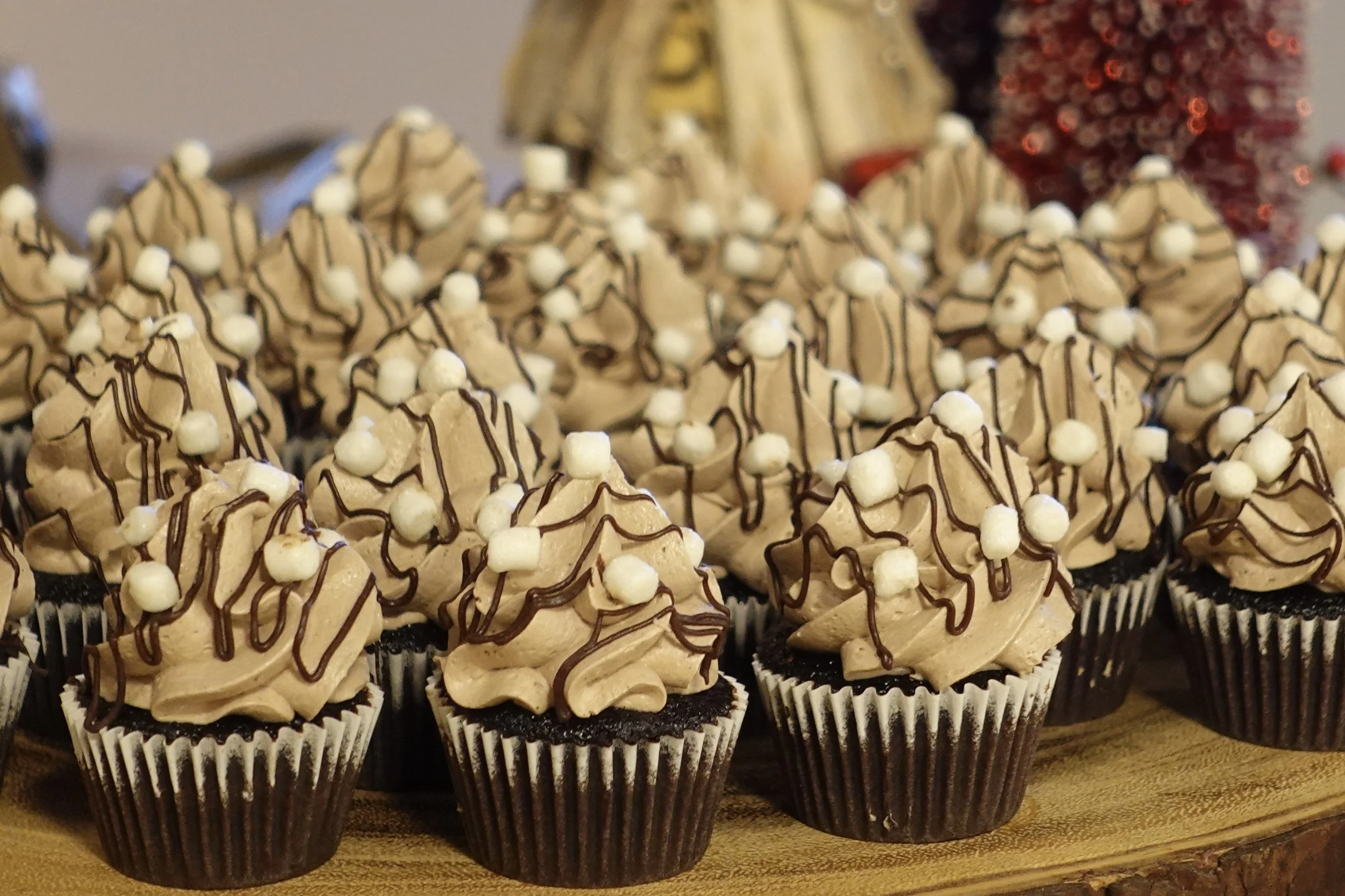 A group of decorated cupcakes with chocolate drizzle, topped with small white candies, arranged on a wooden surface.