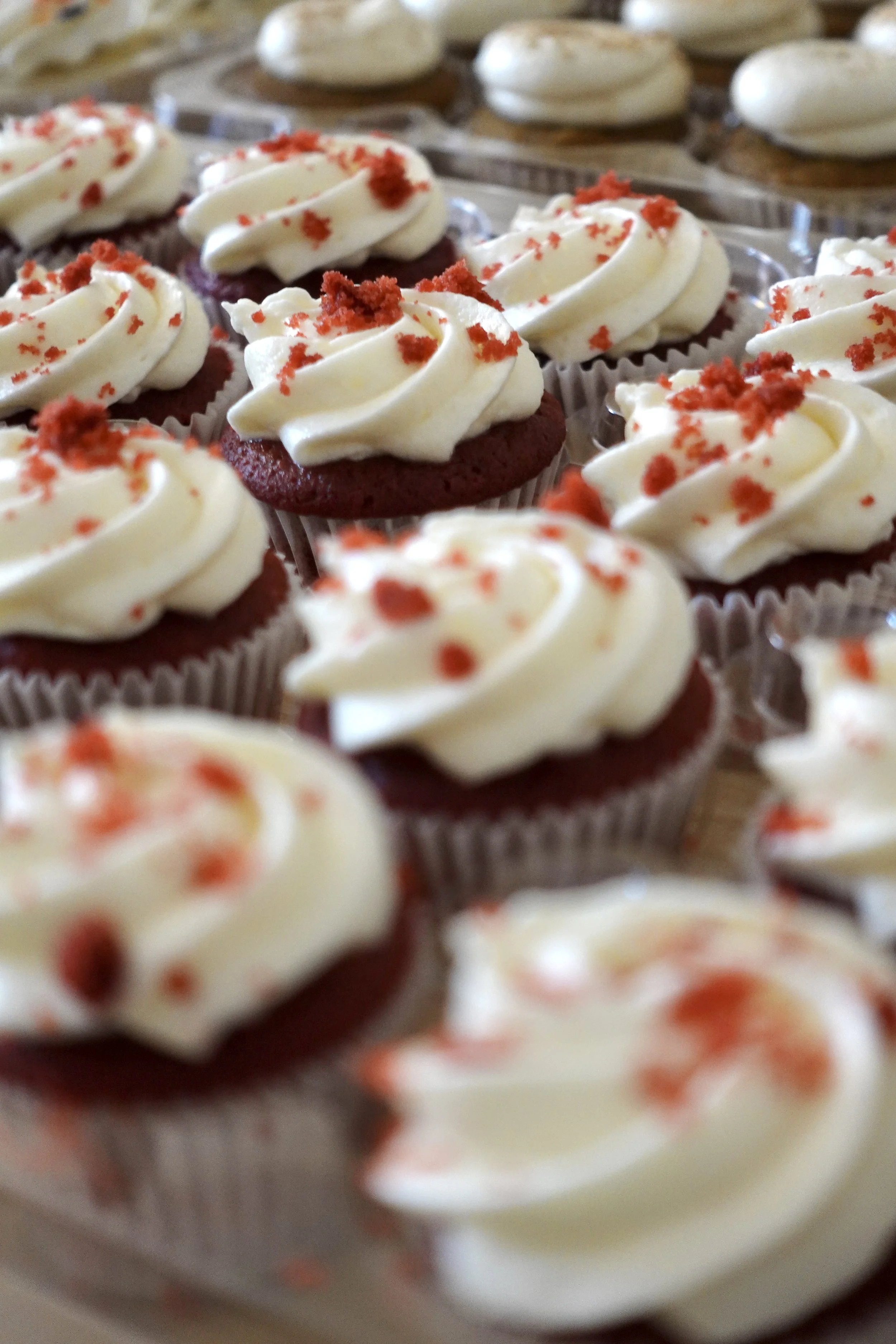 Close-up of red velvet cupcakes with cream cheese frosting and red sprinkles on top.