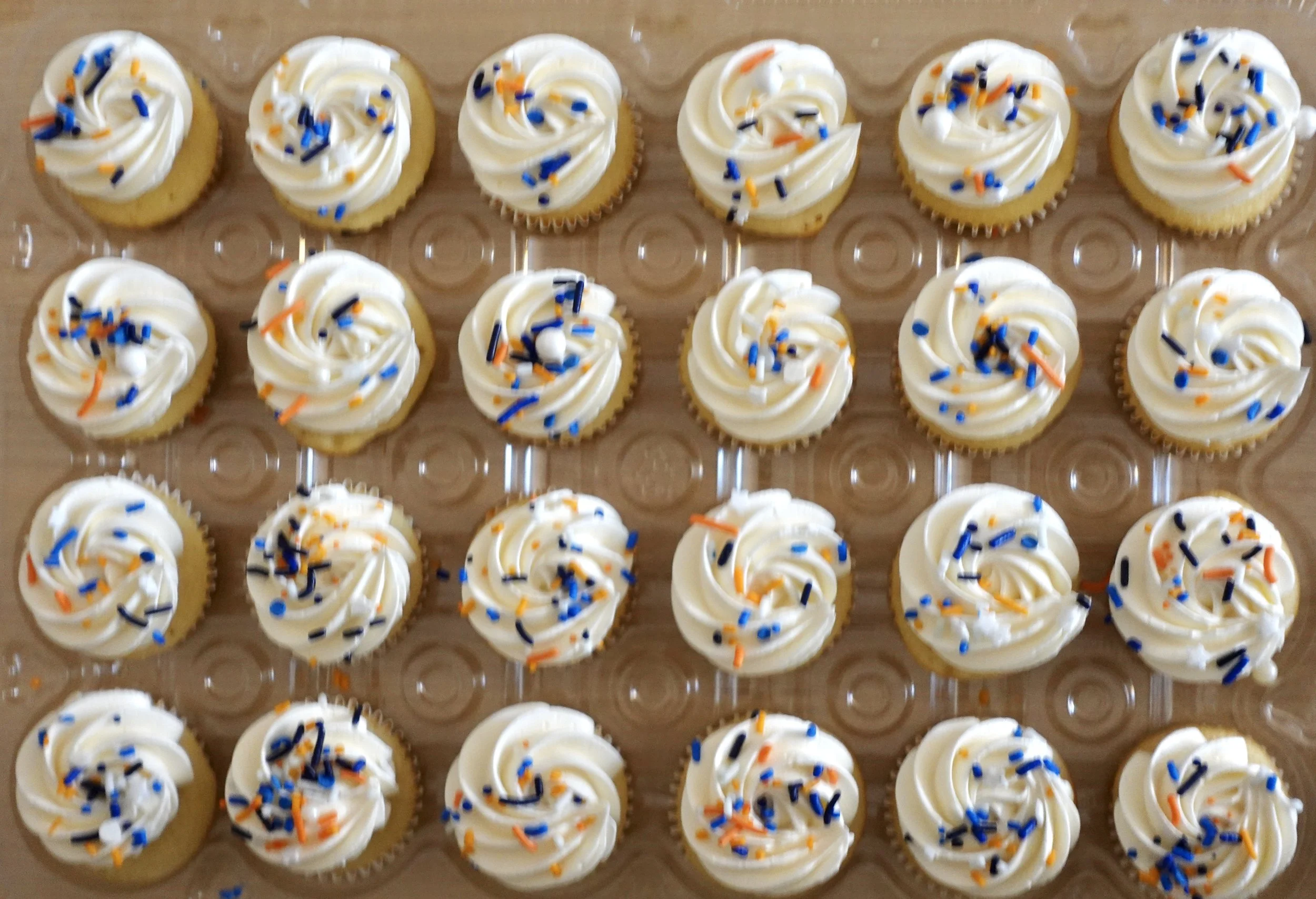 A tray of cupcakes decorated with white frosting and colorful sprinkles.