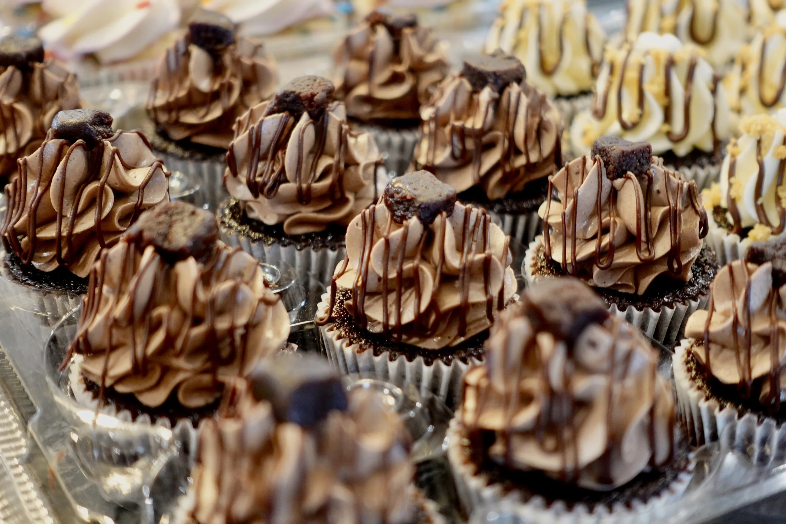 Assorted cupcakes with chocolate and vanilla frosting topped with chocolate drizzle and small brownie pieces.