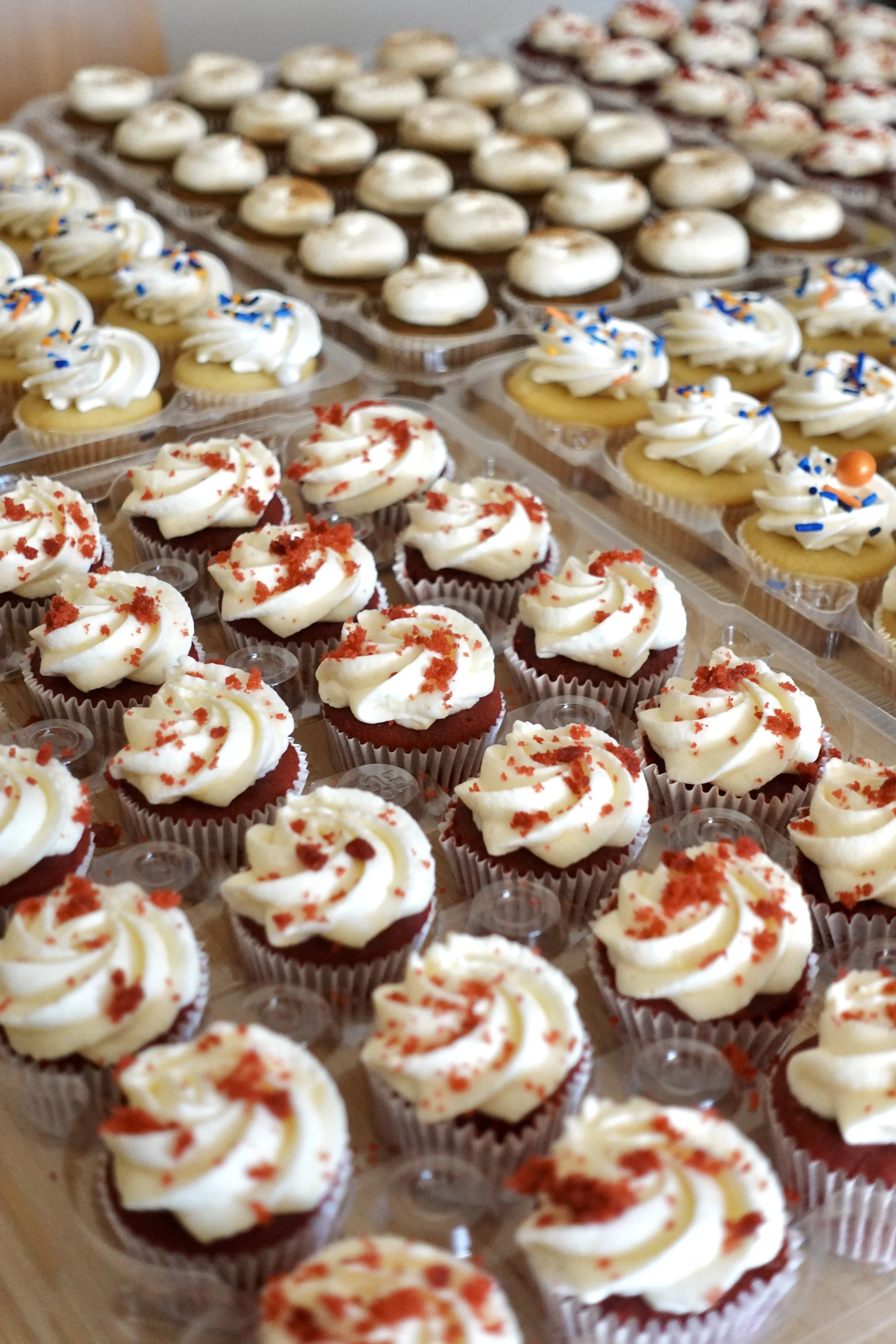 A tray of decorated cupcakes with white frosting and red and blue sprinkles, and a row of mini pies with white frosting and red sprinkles.