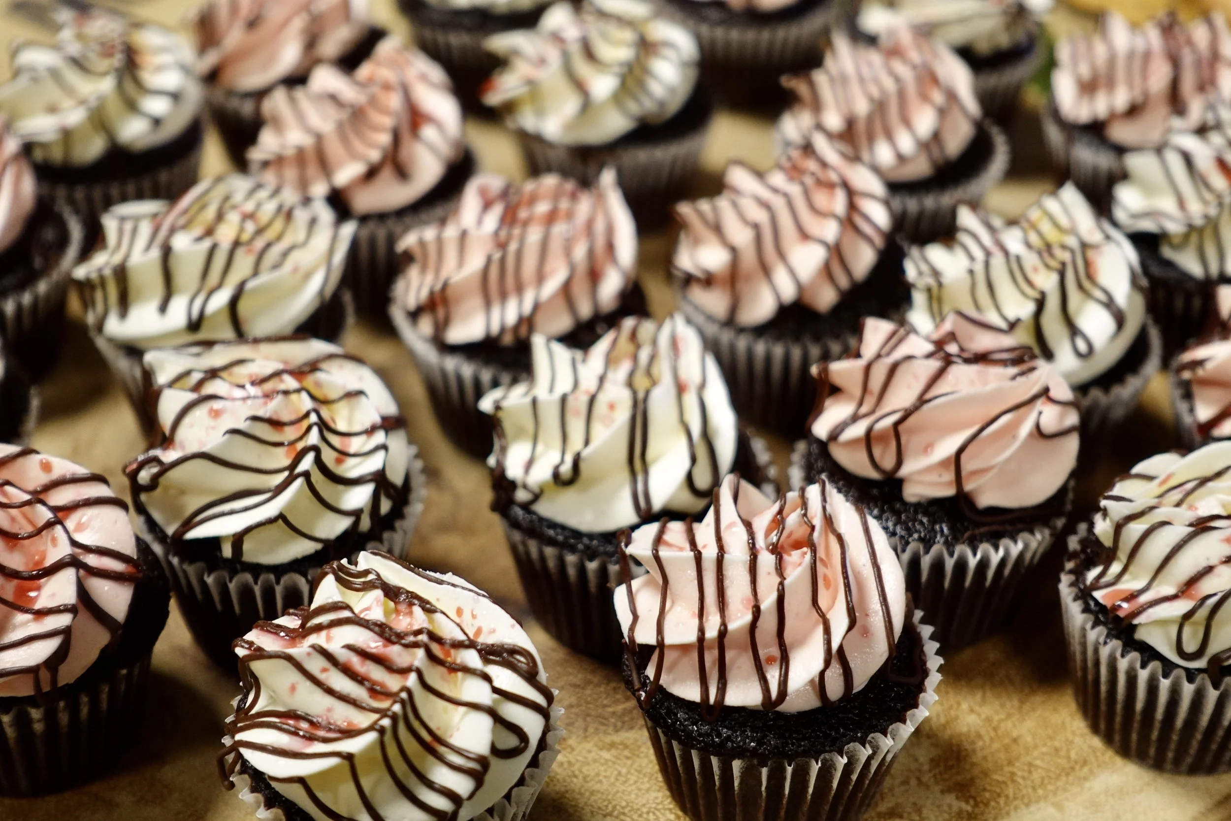 Chocolate cupcakes with pink and white frosting and drizzled chocolate on top, arranged on a flat surface.