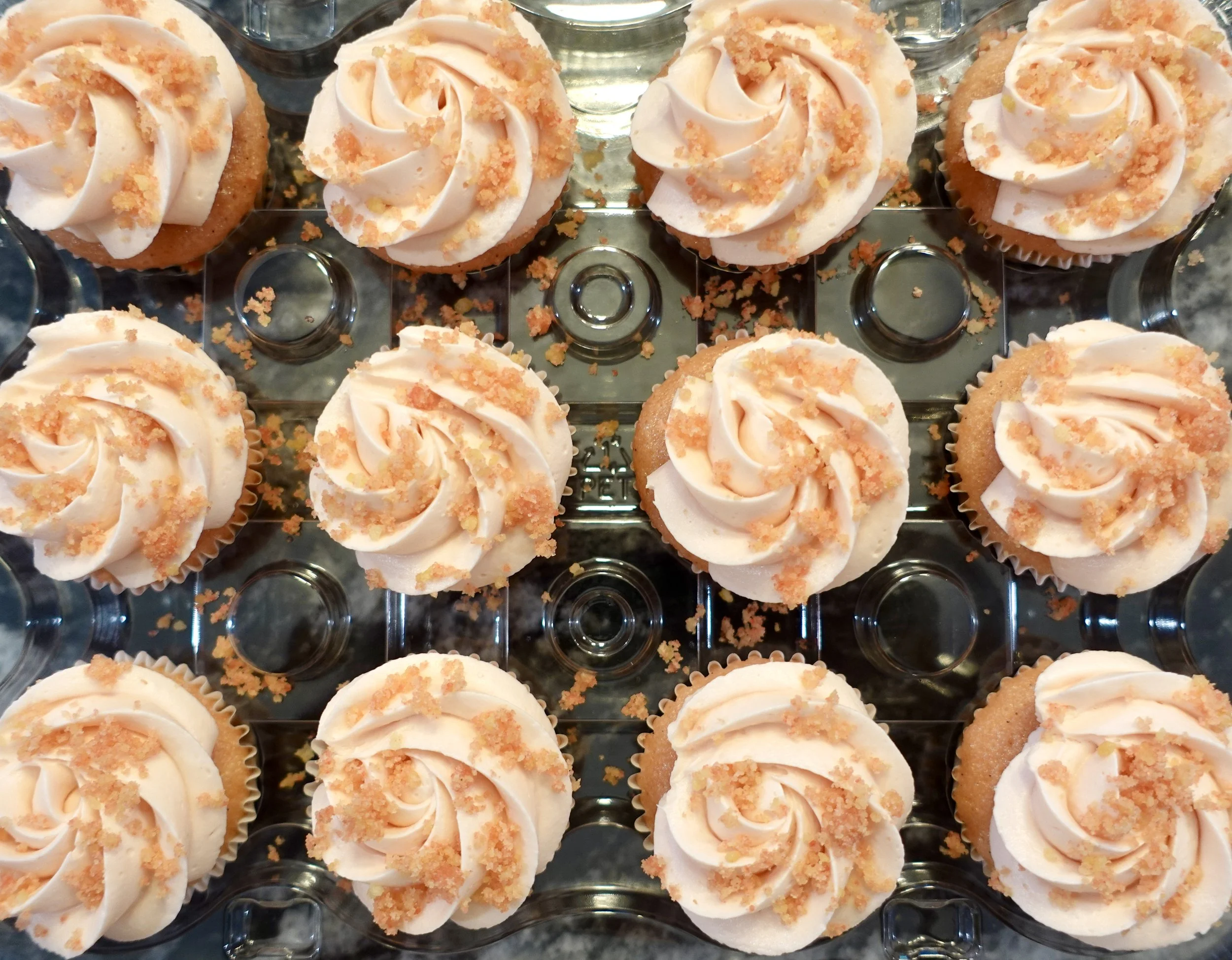 A tray of cupcakes with white frosting swirls and orange crumbs on top.