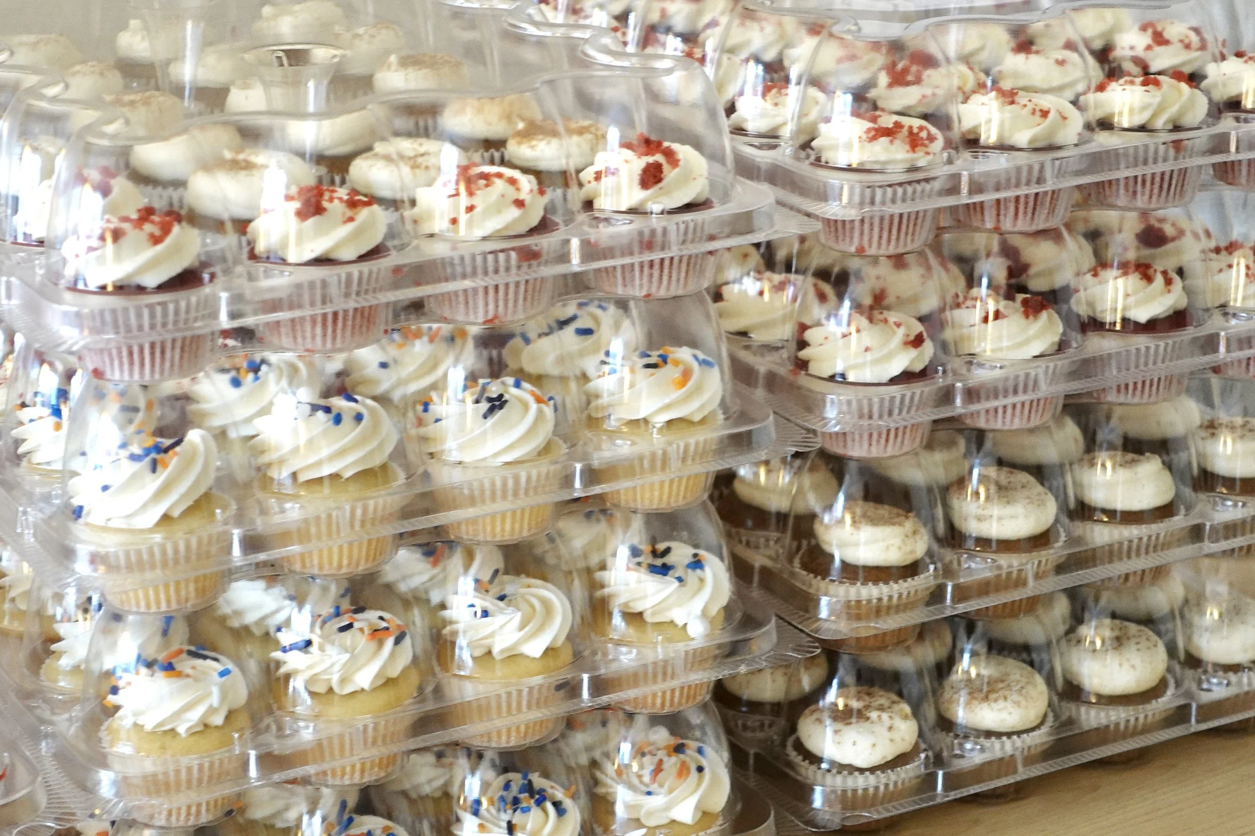 Multiple trays of decorated cupcakes with various frosting and sprinkles, stacked on top of each other.