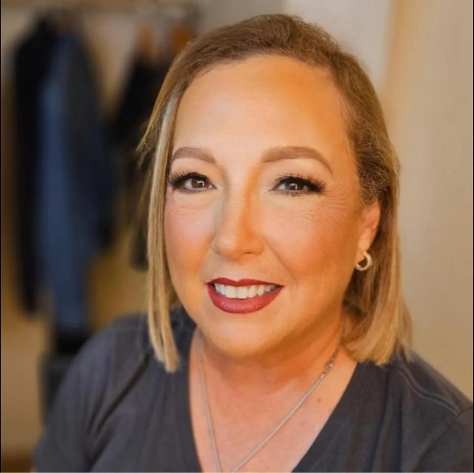 A woman, Melanie Rice, with blonde hair, makeup, red lipstick, wearing earrings and a necklace, smiling at the camera.