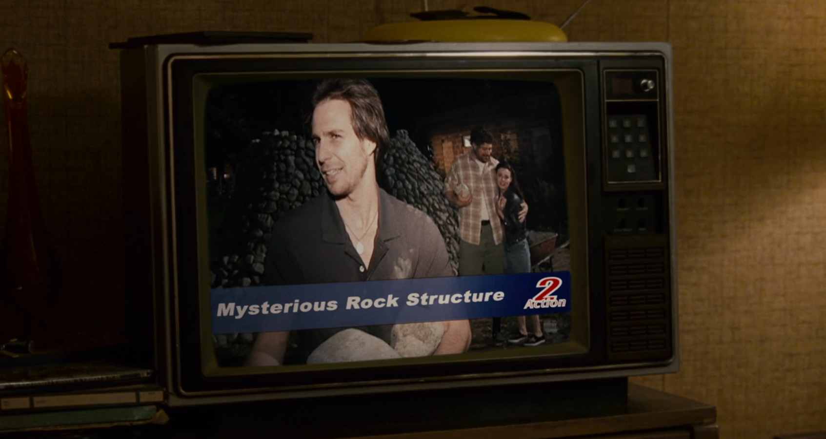 Sam Rockwell on a tube TV with a chyron that reads "Mysterious Rock Structure"
