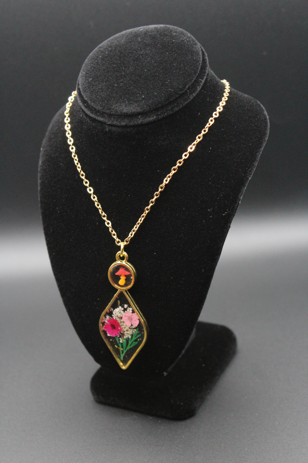 A beautiful golden framed necklace with flowers encased in clear resin inside.