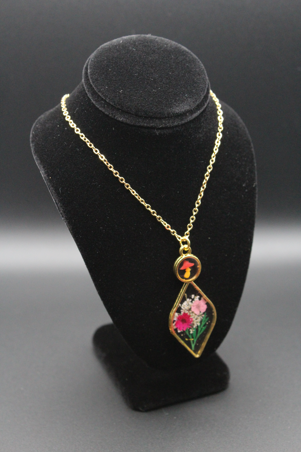 A beautiful golden framed necklace with flowers encased in clear resin inside.