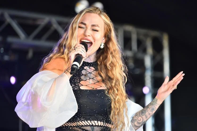A woman sings passionately on stage, holding a microphone, with her eyes closed and an expressive gesture.