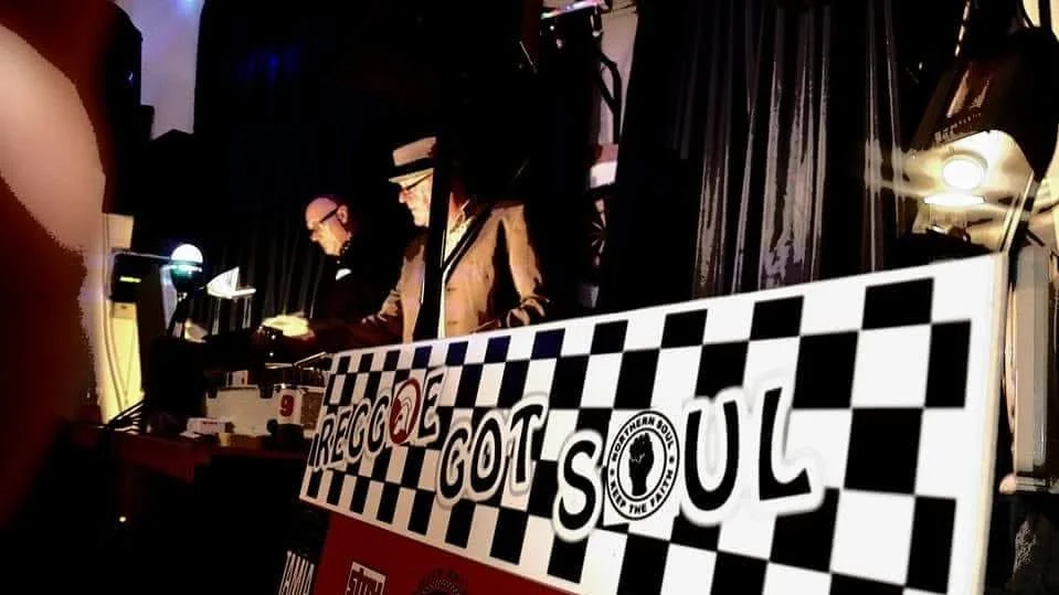 Three musicians, possibly DJs or electronic music artists, performing on stage with a sign that reads 'RECORD GOT SOUL' in front of a dark curtain background.