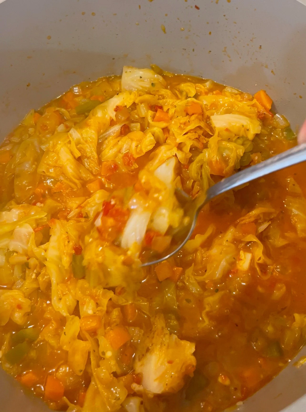 A spoon scooping up cooked cabbage and vegetable soup or stew with visible cabbage, carrots, and broth.