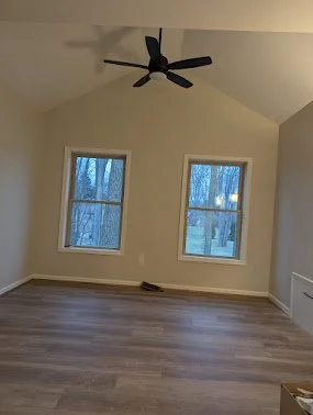 Empty room with two windows, a ceiling fan, light-colored walls, and wood flooring.