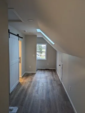 Empty room with hardwood floors, a window, and skylights, under a sloped ceiling.