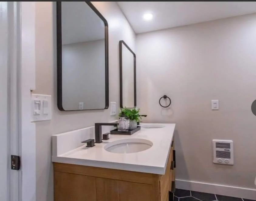 Bathroom vanity with a white countertop, dark faucet, two rectangular mirrors, a small potted plant, and a towel ring.