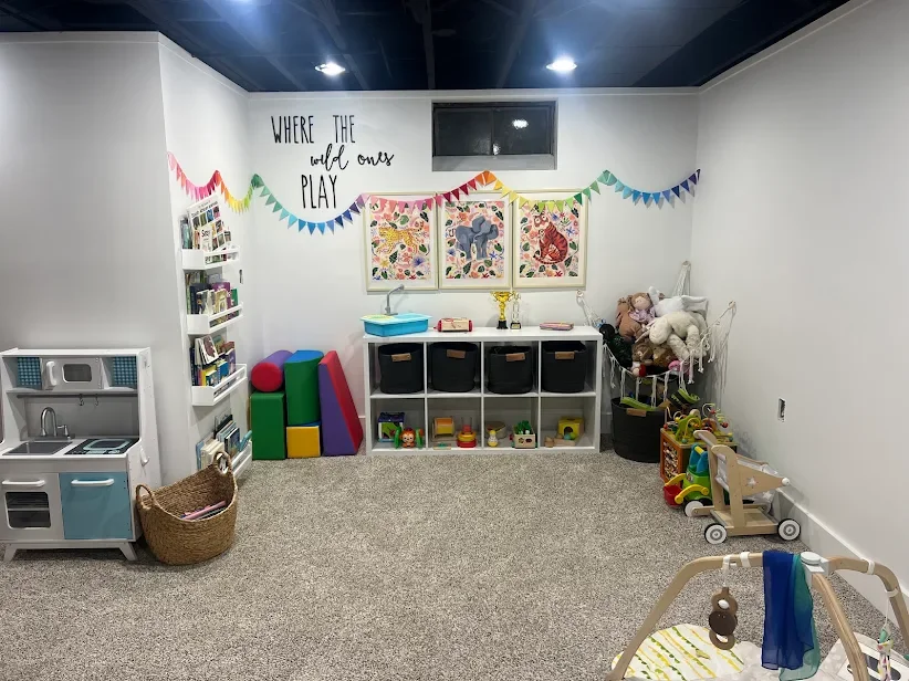 Children's playroom with toys, books, and colorful decorations, including a wall quote 'WHERE THE wild ones PLAY' and framed animal artwork.