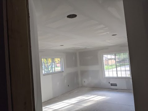 Empty room with unpainted drywall, two windows, and ceiling lights